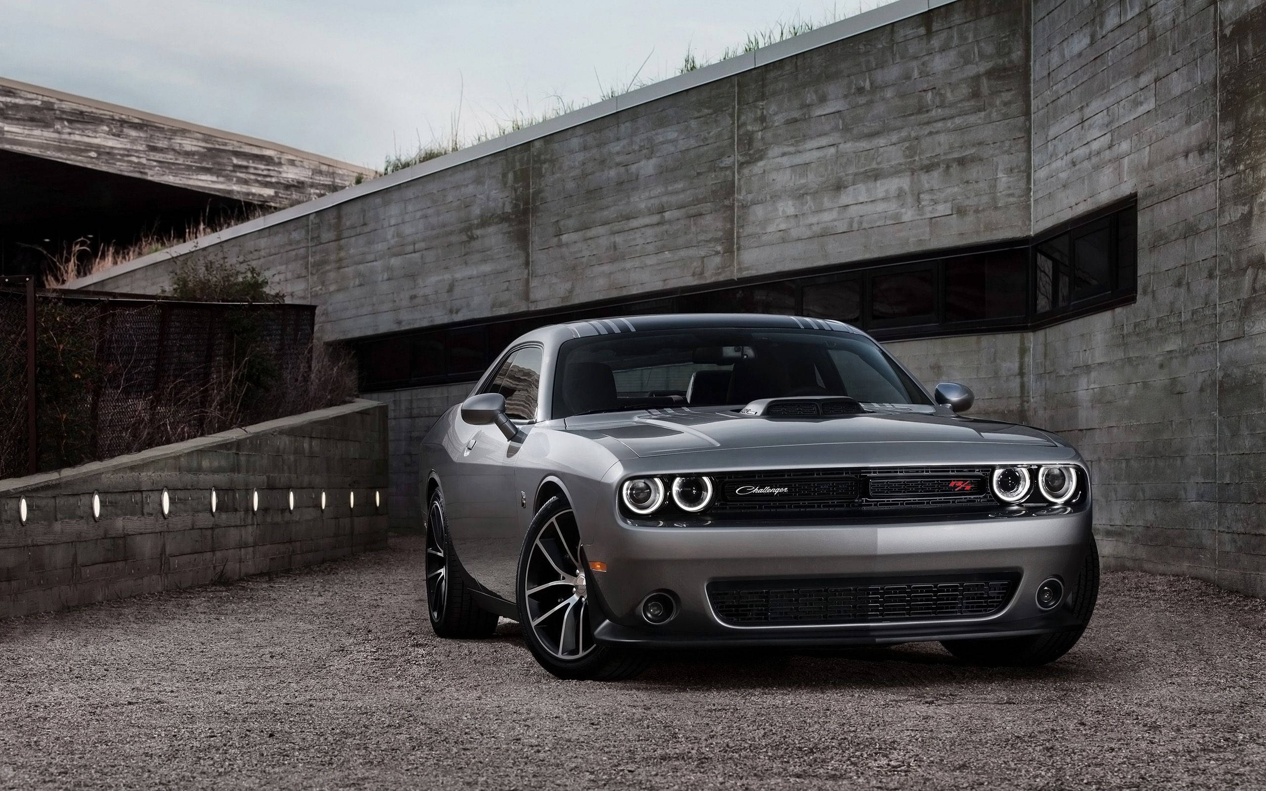 Challenger 桌布 壁紙 — 一架時尚的銀色 Dodge Challenger SRT Hellcat 停泊在碎石上，旁邊是現代混凝土牆，天空多雲。