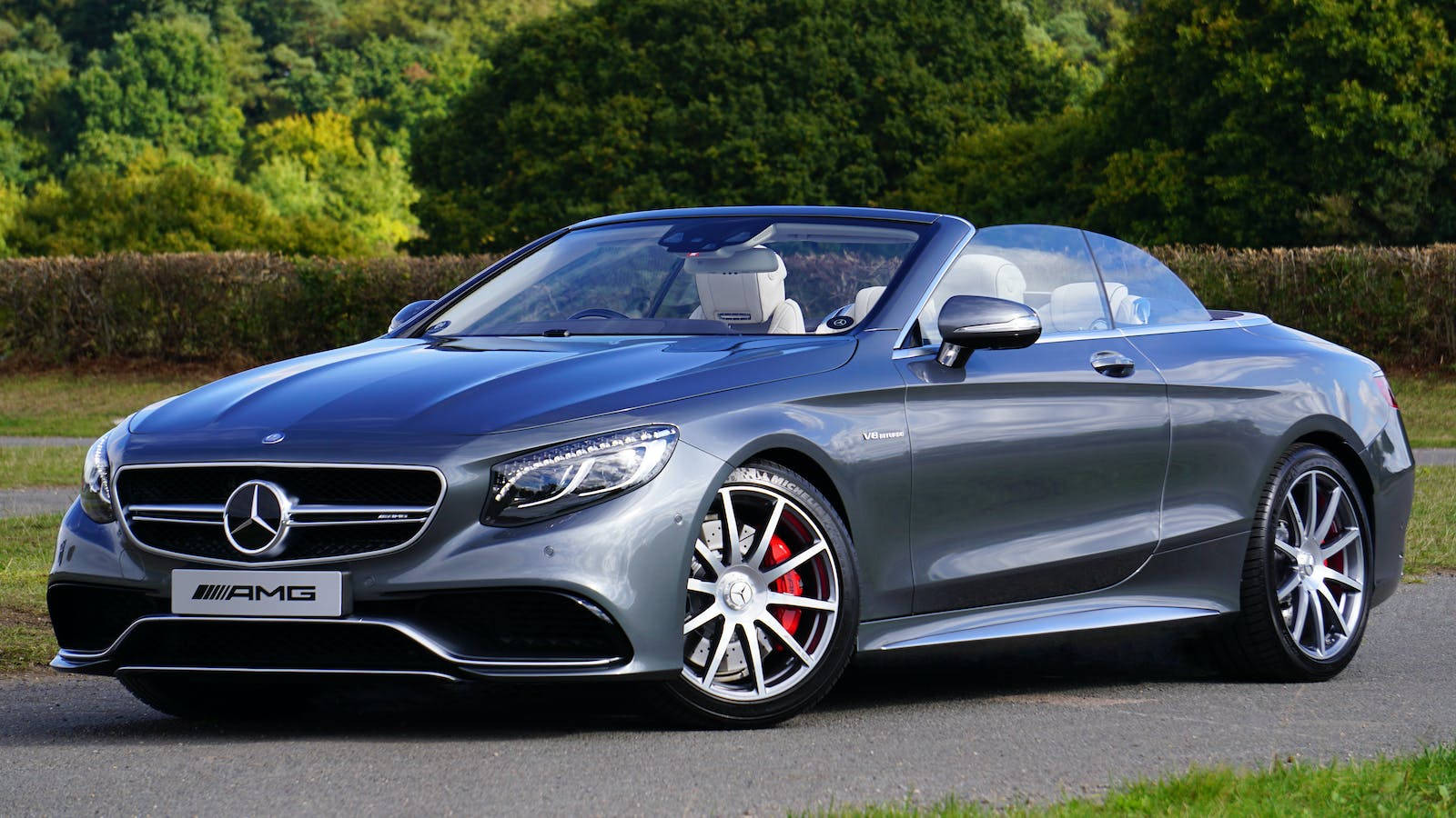 跑車 桌布 壁紙 — 一架時尚的銀色 Mercedes-AMG S63 敞篷車停泊在道路上，背景是茂密的綠色樹木。