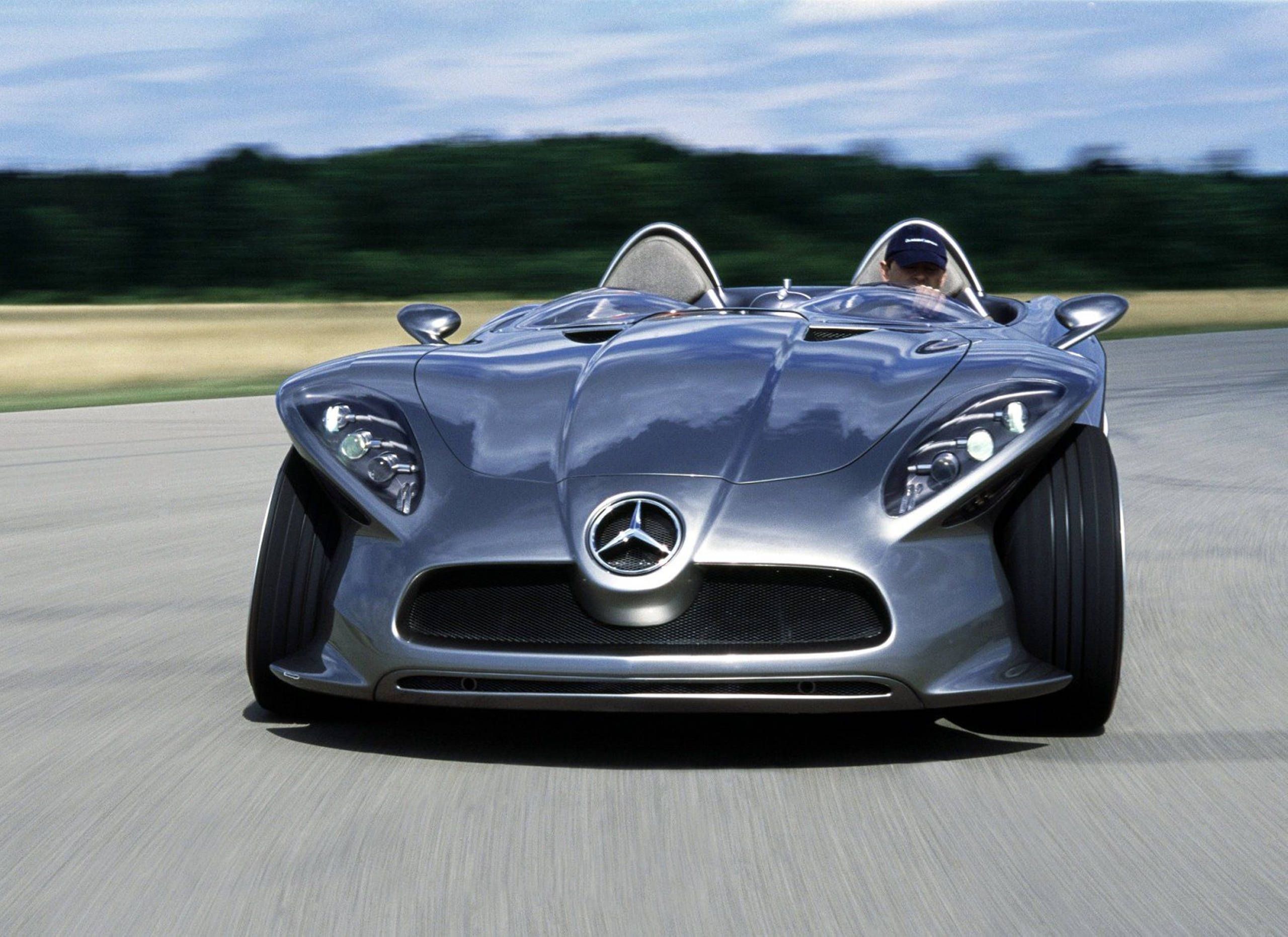 高清 桌布 壁紙 — 一架時尚的銀色 Mercedes-Benz 概念車在鋪砌的賽道上疾馳，背景是模糊的綠色植物。
