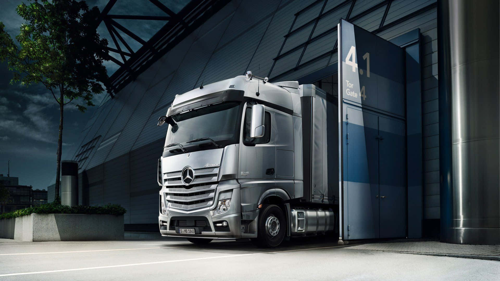 Truck 桌布 壁紙 — 一架時尚的銀色 Mercedes-Benz 半掛卡車停泊在現代工業裝卸區，背景是陰鬱的暮色天空。
