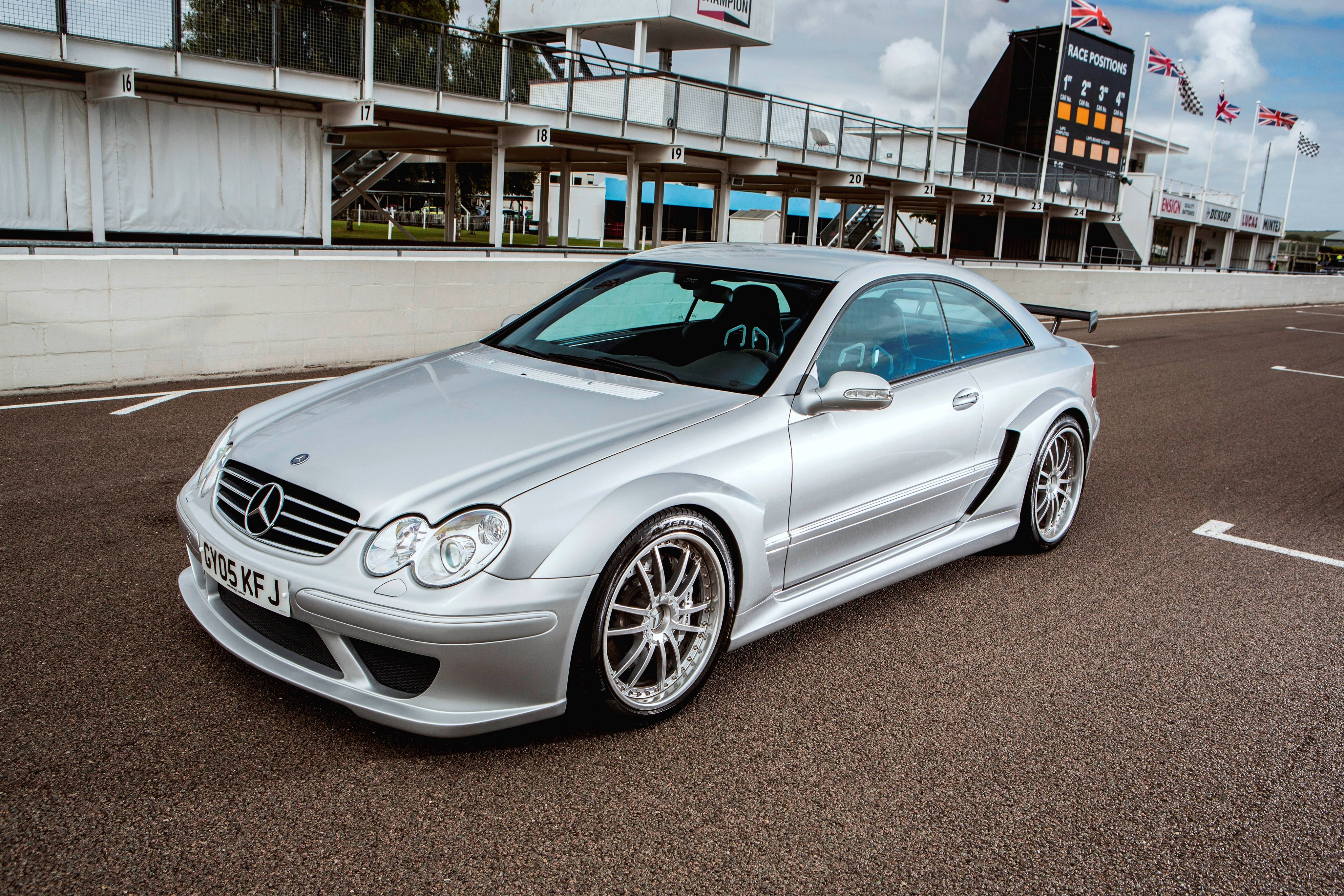 benz 4K 桌布 壁紙 — 一架時尚的銀色 Mercedes-Benz CLK GTR 賽車停泊在賽道上，背景有看台和英國國旗。