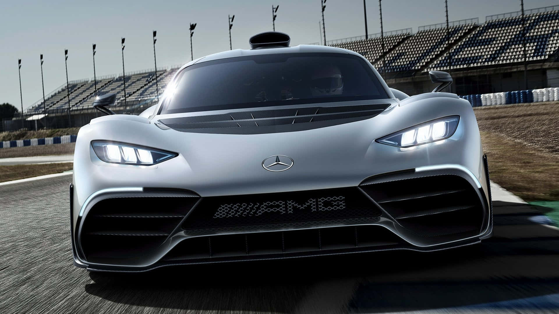 Mercedes 桌布 壁紙 — 一架時尚的銀色 Mercedes-AMG 賽車，車頭燈閃爍，主宰著陽光普照的賽道，其進取的前格柵和空氣動力學設計已準備好迎接高速。