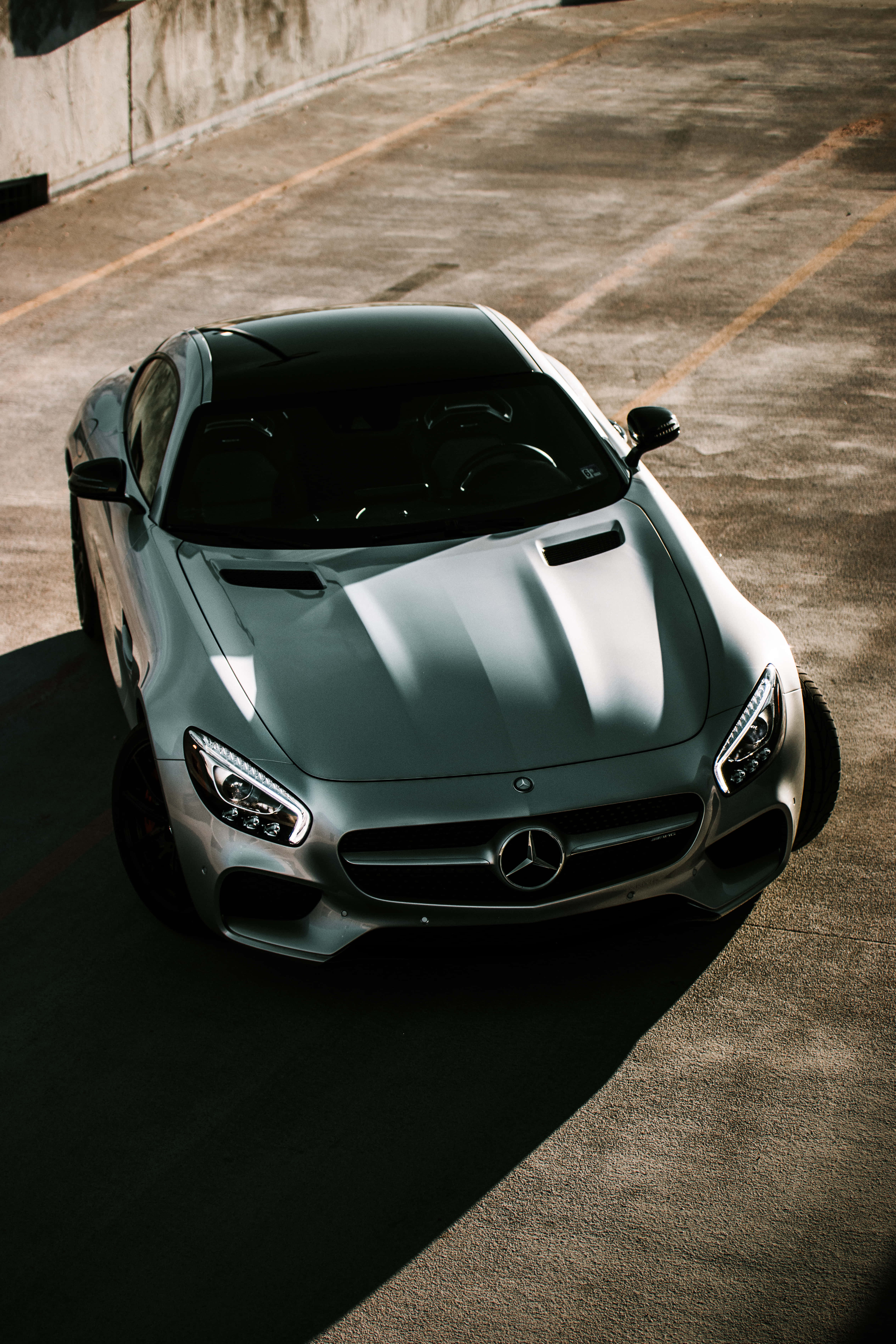 Top View 桌布 壁紙 — 一架時尚的銀色 Mercedes-AMG GT 停泊在陽光普照的混凝土停車場，投下長長的影子。