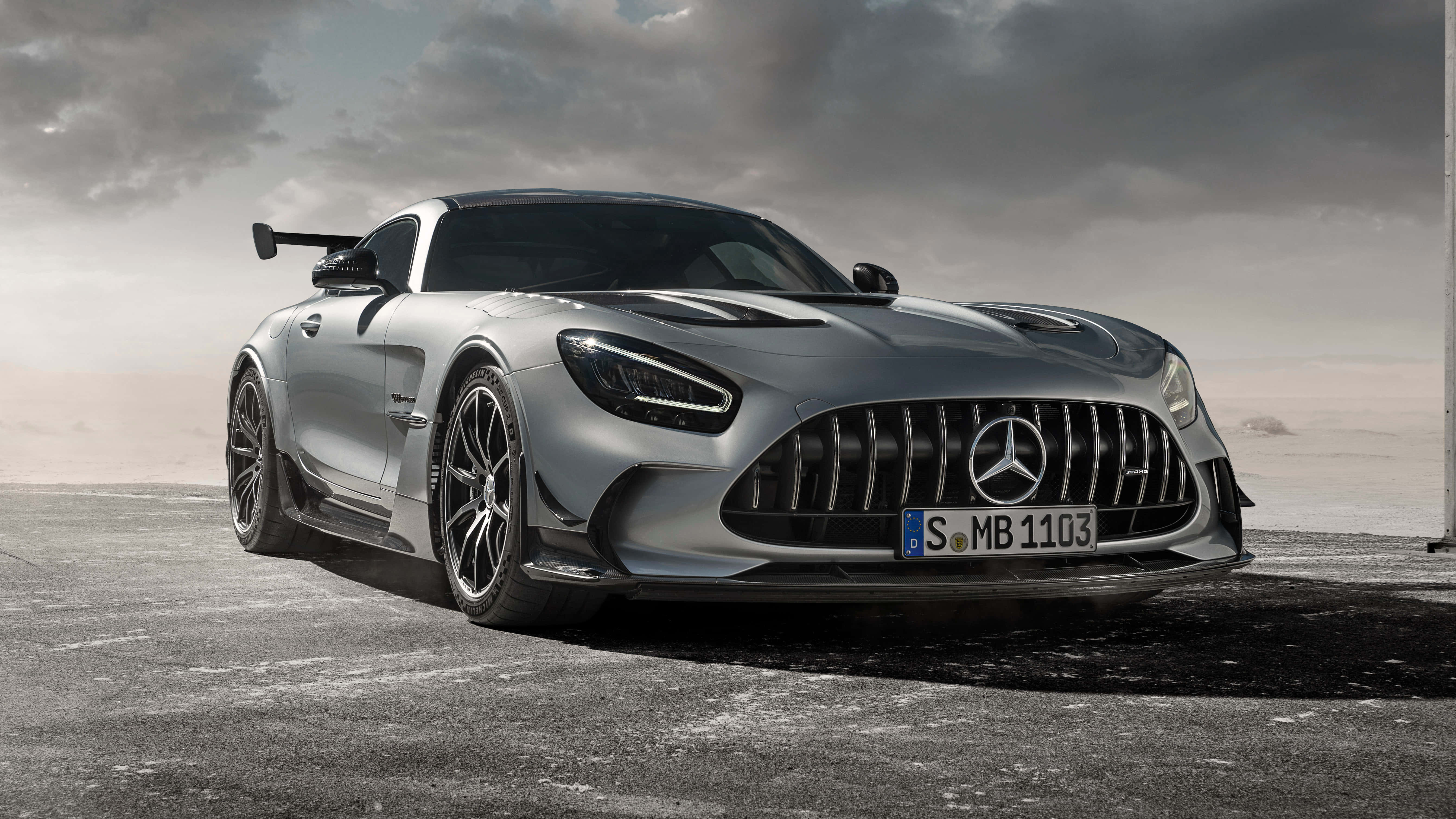 Mercedes Gts 桌布 壁紙 — 一架時尚的銀色 Mercedes-AMG GT Black Series 跑車，帶有大型後擾流板，矗立在混凝土表面上，背景是戲劇性的多雲天空。