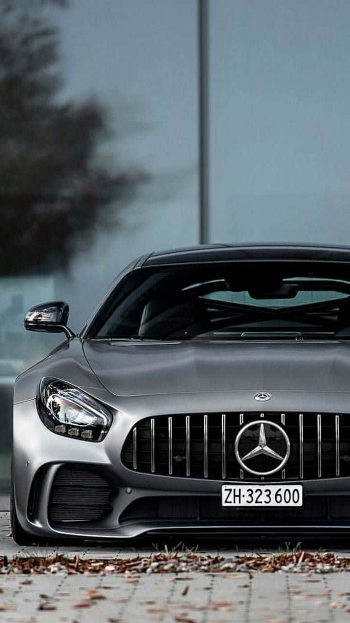 iPhone X Mercedes 桌布 壁紙 — 一架時尚的銀色 Mercedes-AMG GT 停放在鋪砌路面上，周圍散落著落葉，天色陰沉。