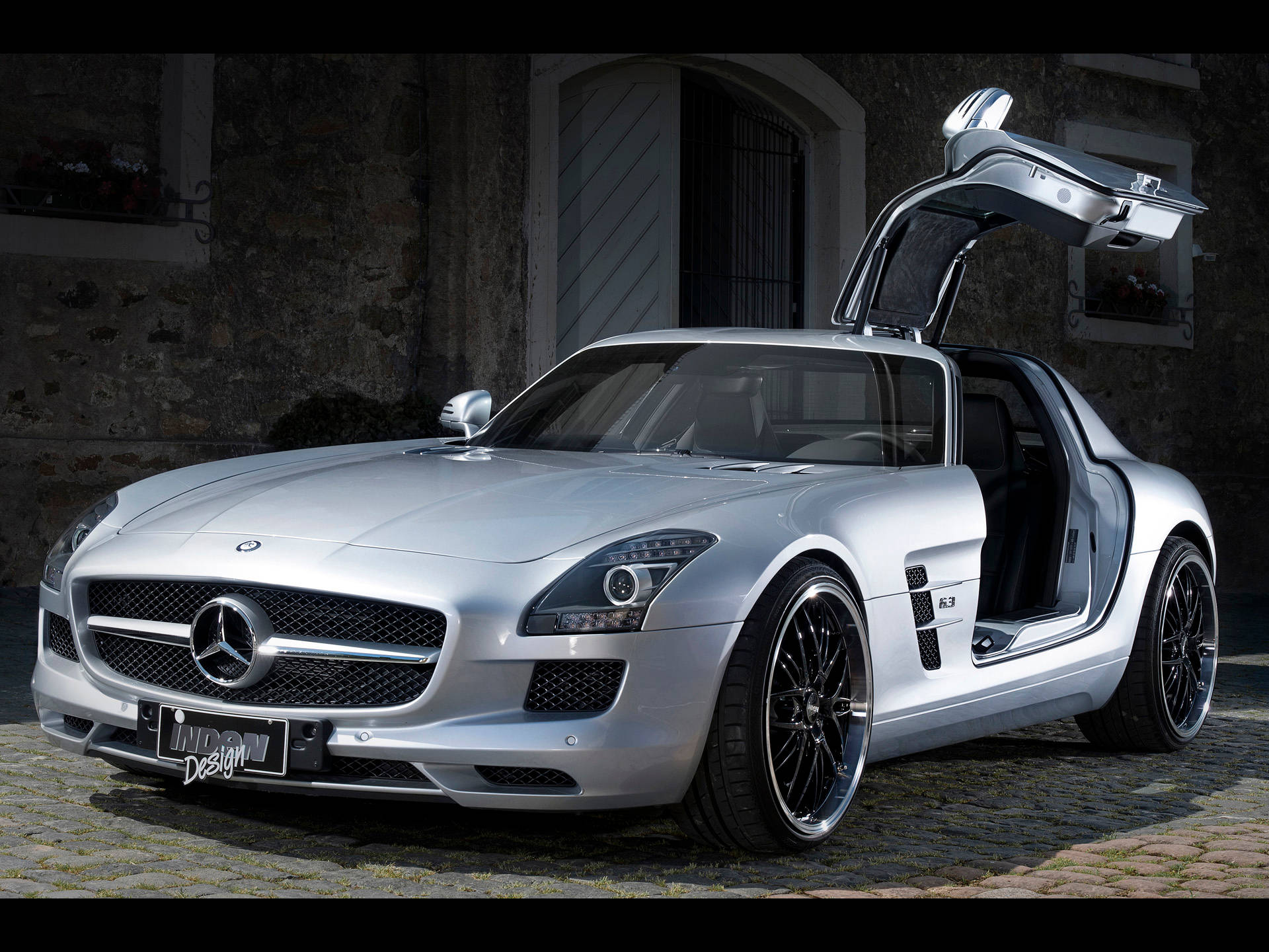 高畫質 賓士 桌布 壁紙 — 一架時尚的銀色 Mercedes SLS AMG 跑車，鷗翼車門打開，停在石頭建築前的鵝卵石路上。