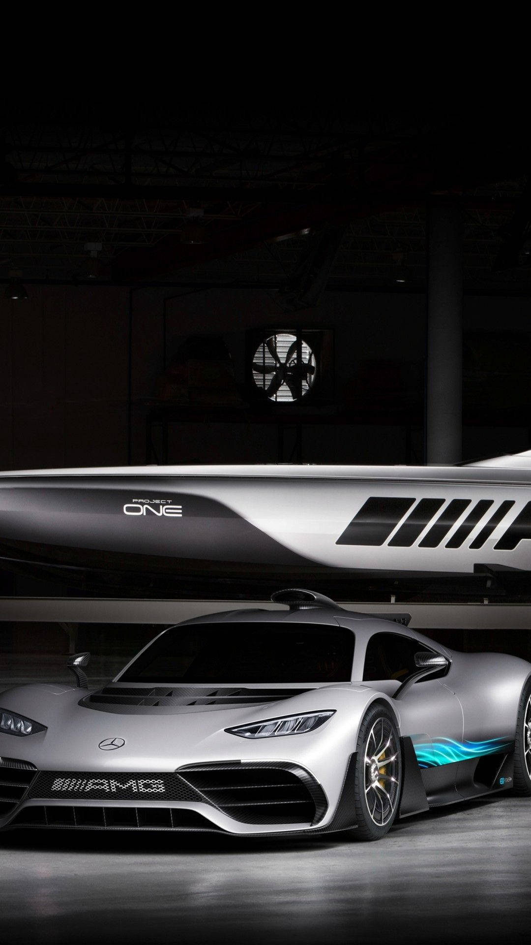 賓士 iPhone 桌布 壁紙 — 一架時尚的銀色 Mercedes-AMG Project One 超跑在昏暗的工業機庫中，於相配的船隻下方，在攝影棚燈光下閃閃發光。