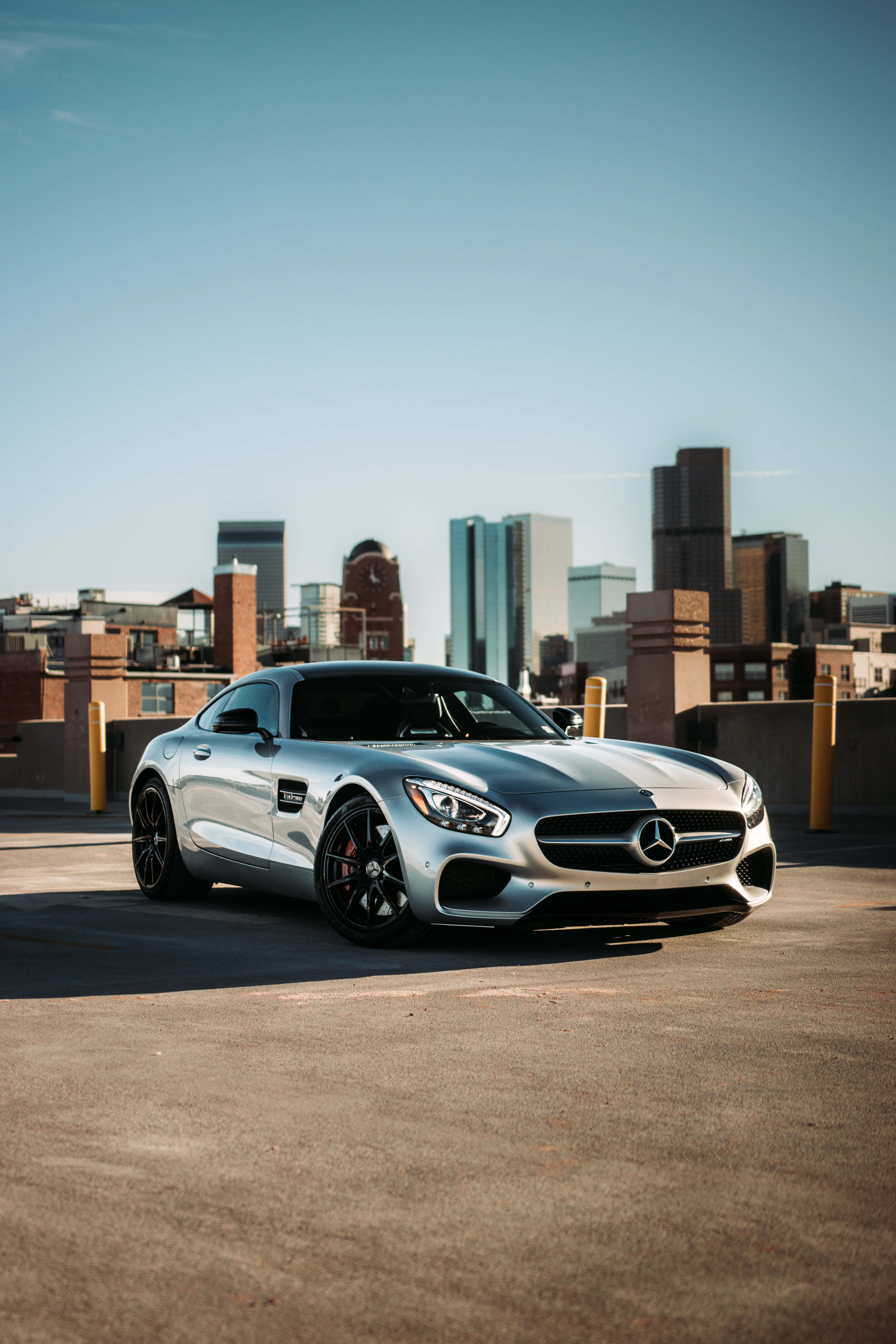 美學 桌布 壁紙 — 一架時尚的銀色 Mercedes-AMG GT 跑車停放在屋頂上，背景是晴朗藍天下的城市天際線。