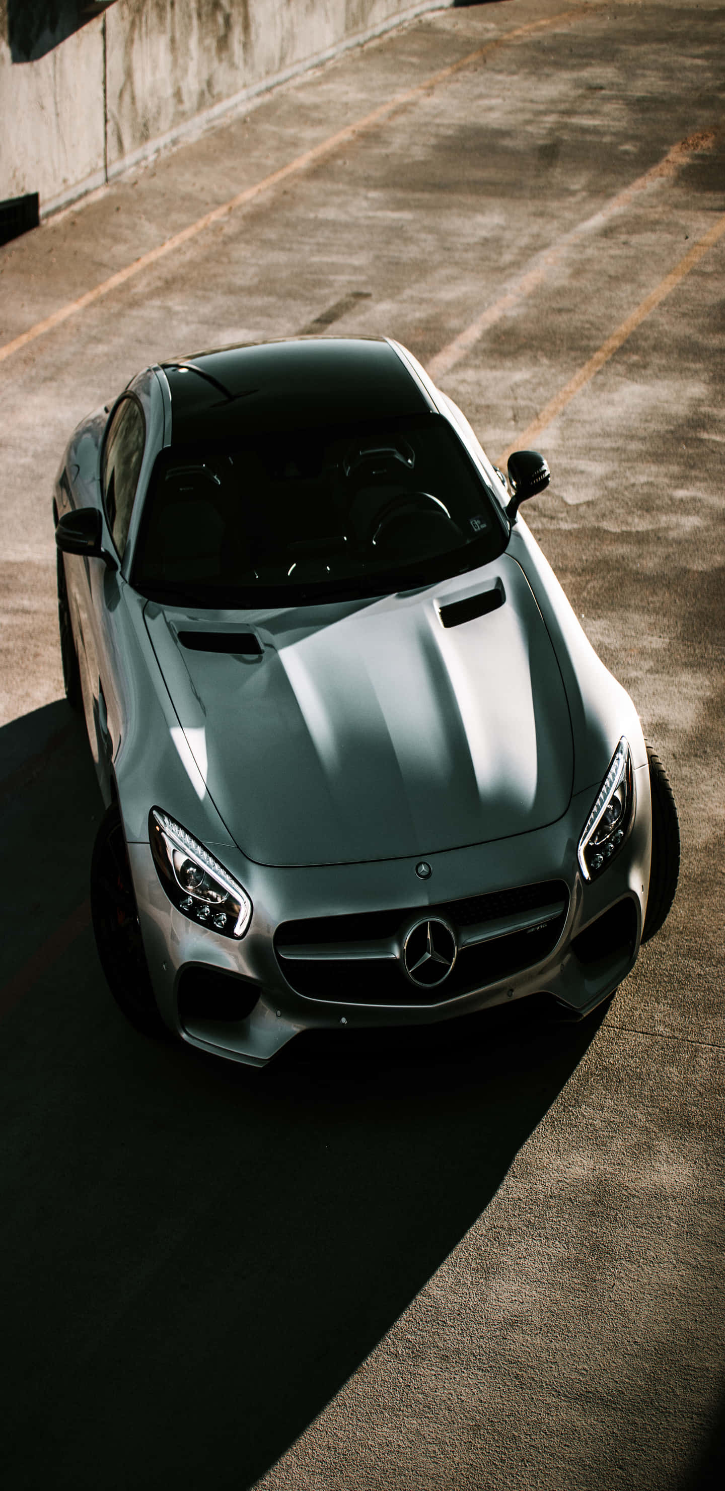 Car Phone 桌布 壁紙 — 一架時尚的銀色 Mercedes-AMG GT 停放在陽光普照的混凝土停車場，投射出銳利的陰影。