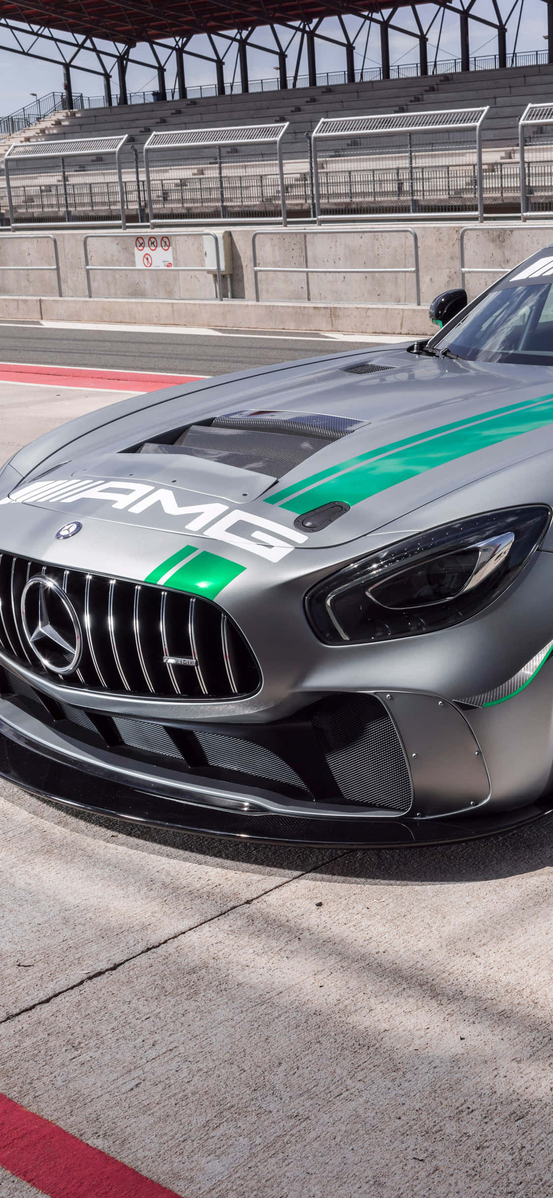 iPhone X Amg Gt-r 桌布 壁紙 — 一架時尚的銀色AMG賽車，帶有綠色條紋，停在混凝土賽道上，在明亮的日光下。