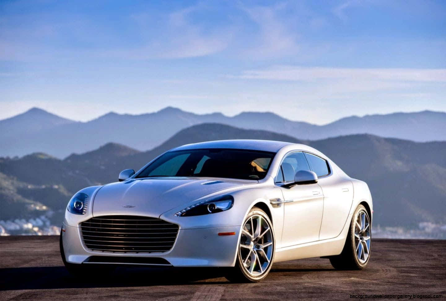 Aston Martin Rapide S 桌布 壁紙 — 一架時尚的銀色Aston Martin跑車停泊在懸崖上，俯瞰著遠處的山脈，天空清澈湛藍。