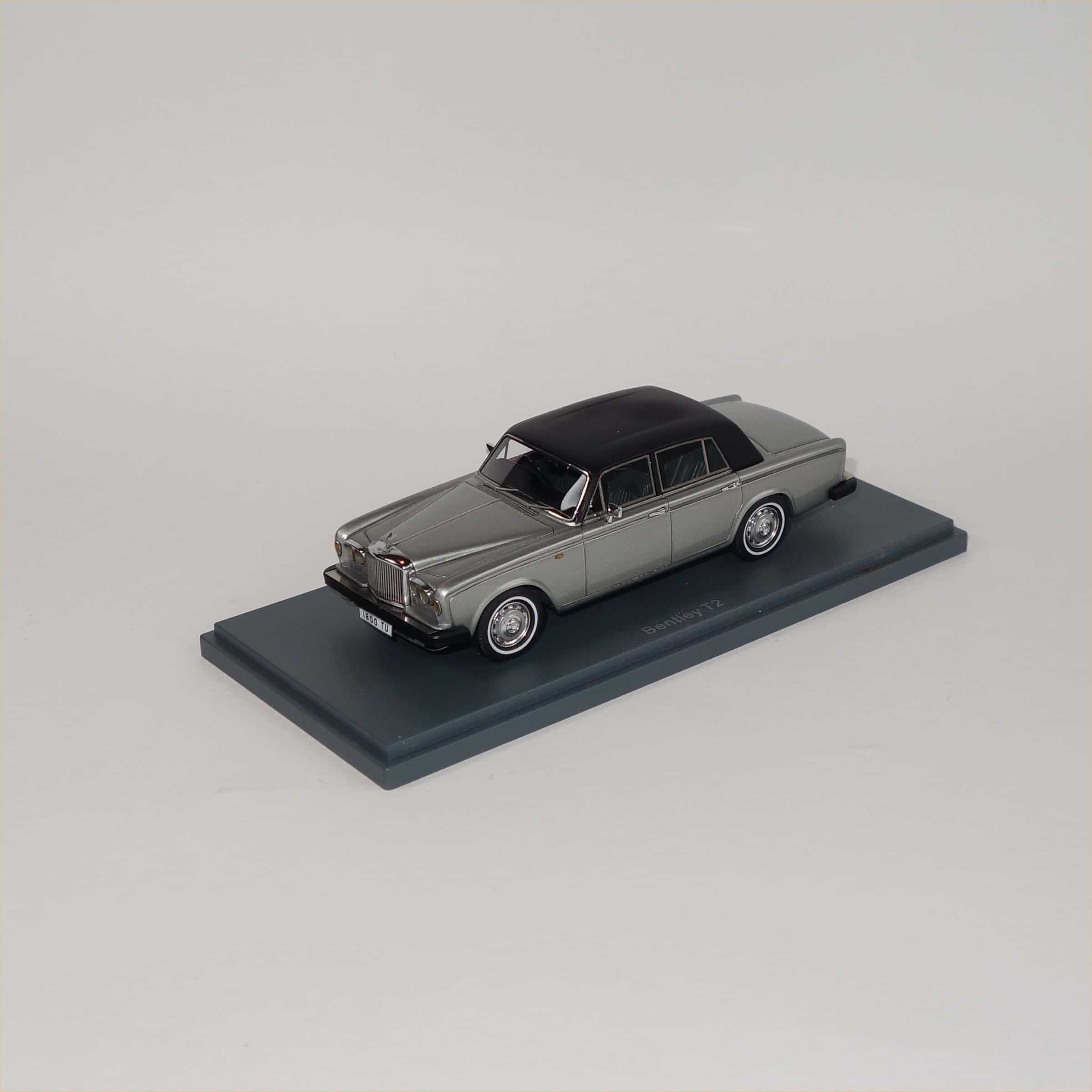 Bentley T2 桌布 壁紙 — 一架時尚的銀色Bentley T2模型車，黑色車頂，放置在深灰色展示底座上，背景為純白色。