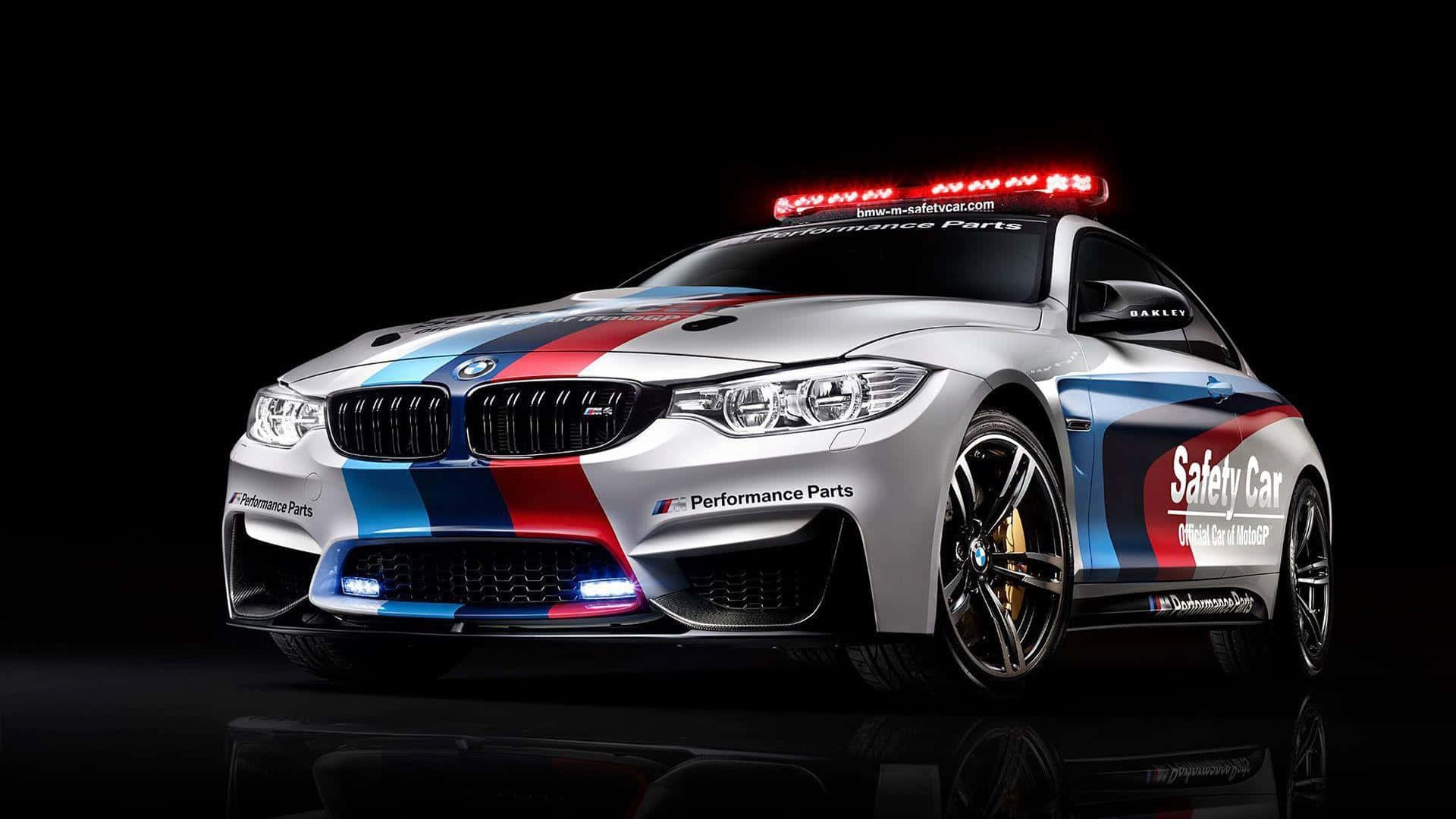 Safety Car 桌布 壁紙 — 一架時尚的銀色BMW M4賽車，帶有紅、藍、白賽車條紋和閃爍的紅燈，置於黑色反光表面上。