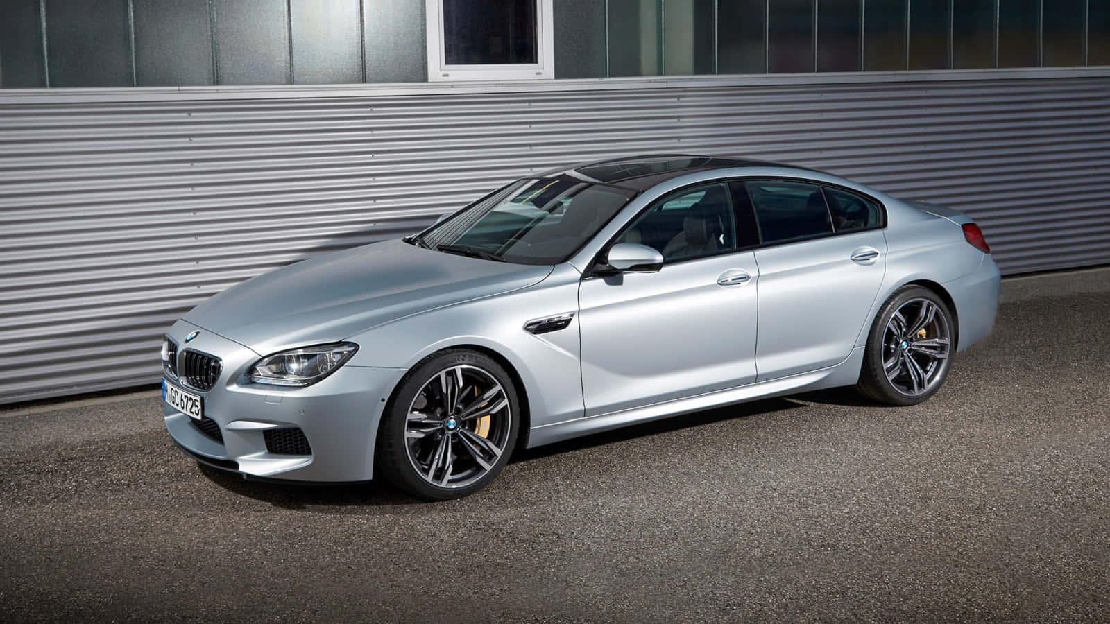 Bmw M6 桌布 壁紙 — 一架時尚的銀色BMW M6跑車在明亮的日光下停靠在波紋金屬牆旁。