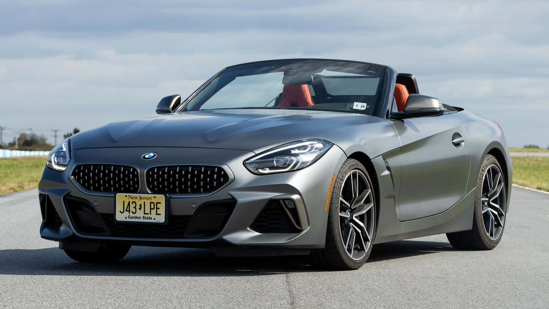 Bmw Z4 桌布 壁紙 — 一架時尚的銀色BMW Z4敞篷跑車停放在開闊的道路上，天空多雲，可見橙色內飾座椅。