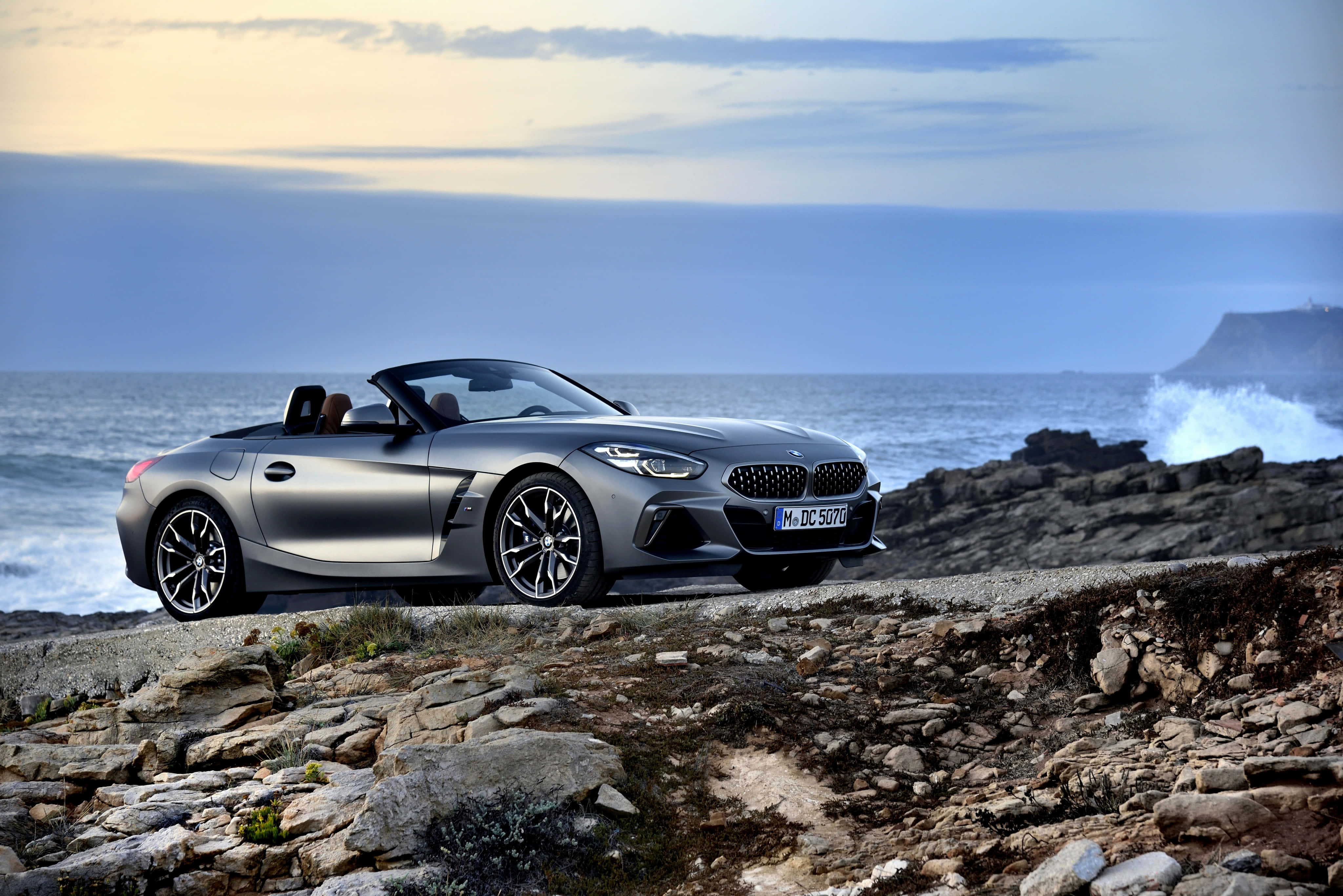 Bmw Z4 桌布 壁紙 — 一架時尚的銀色BMW Z4敞篷跑車停泊在崎嶇的海岸懸崖上，俯瞰著黃昏時分洶湧的海浪。