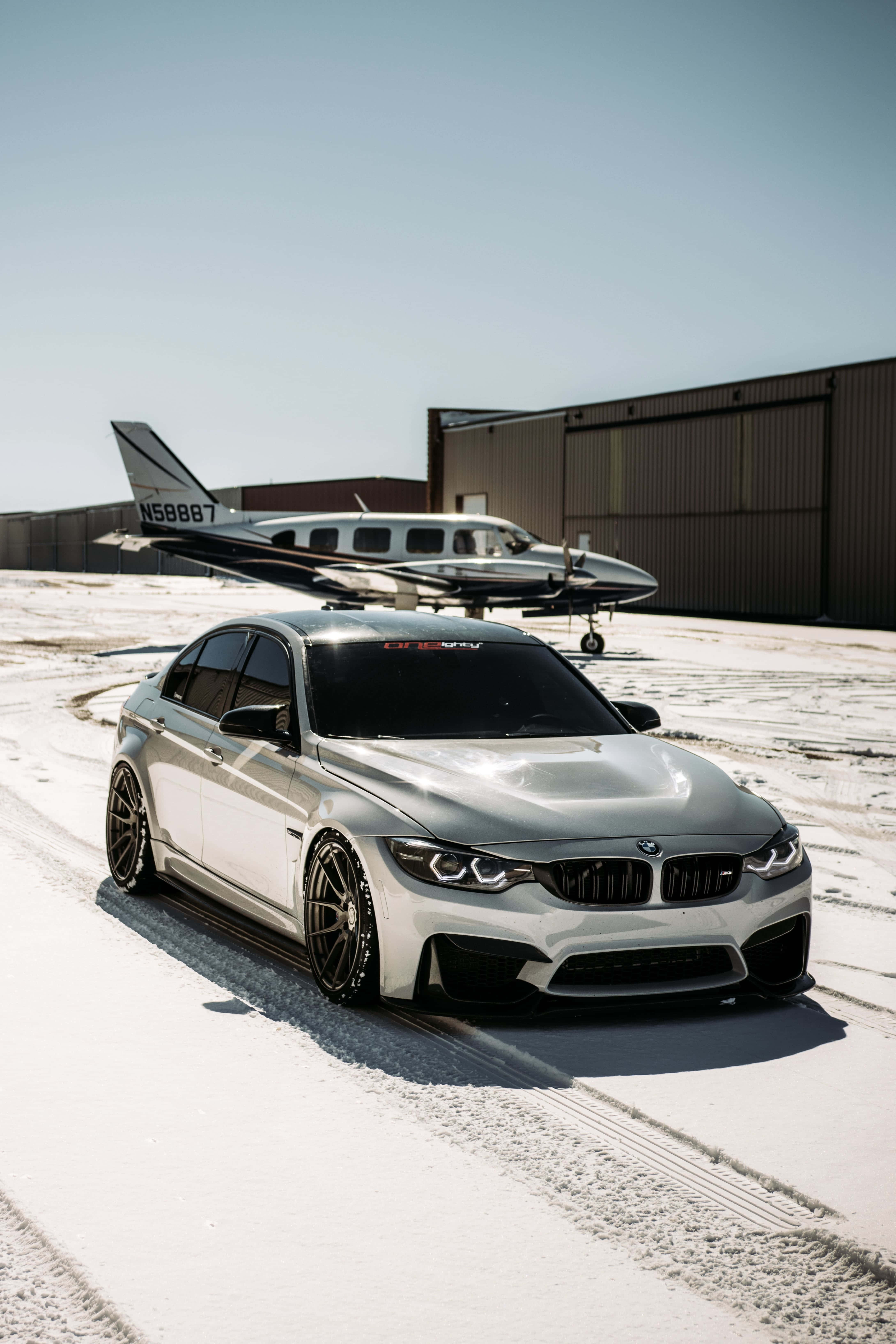 Best M Series 桌布 壁紙 — 一架時尚的銀色BMW跑車停放在積雪的停機坪上，旁邊是一架小型私人飛機，天空湛藍清澈。