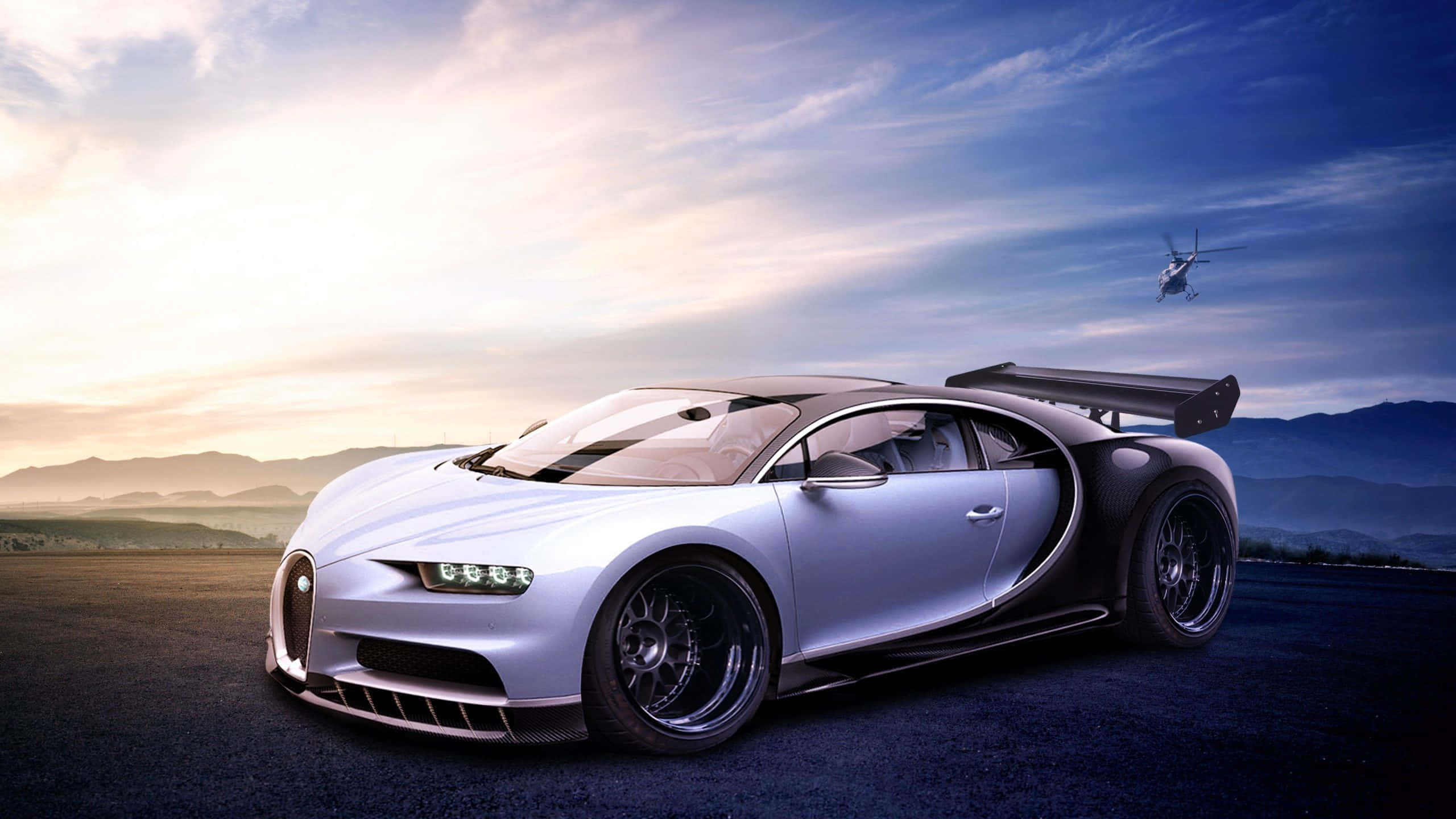 Best Bugatti 桌布 壁紙 — 一架時尚的銀色Bugatti Chiron跑車停泊在日落時分的黑暗道路上，背景有山脈和天空中的直升機。