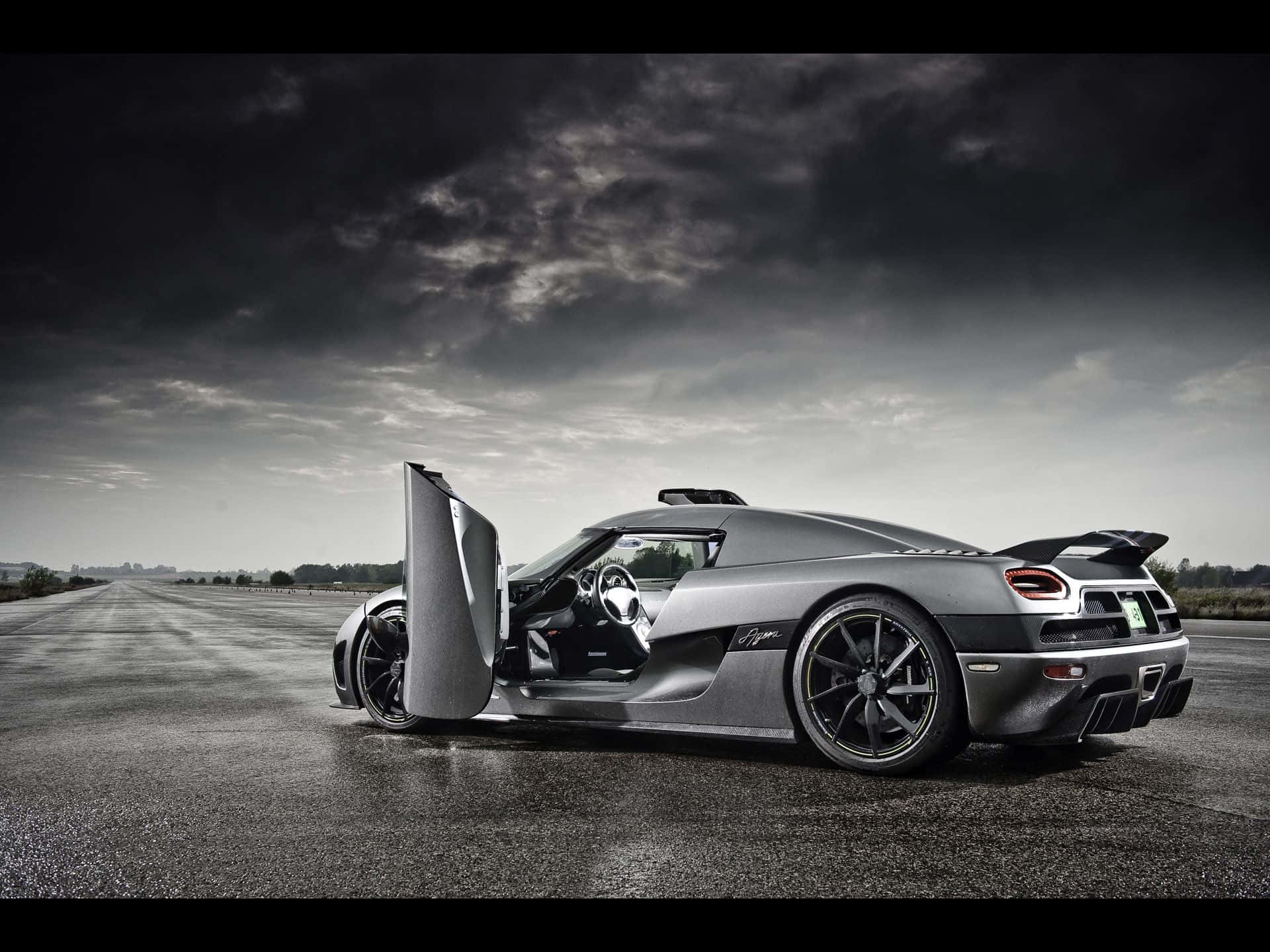 Cool Car 桌布 壁紙 — 一架時尚的銀色Koenigsegg Agera超跑，剪刀門打開，停在空蕩的瀝青路上，背景是戲劇性的多雲天空。