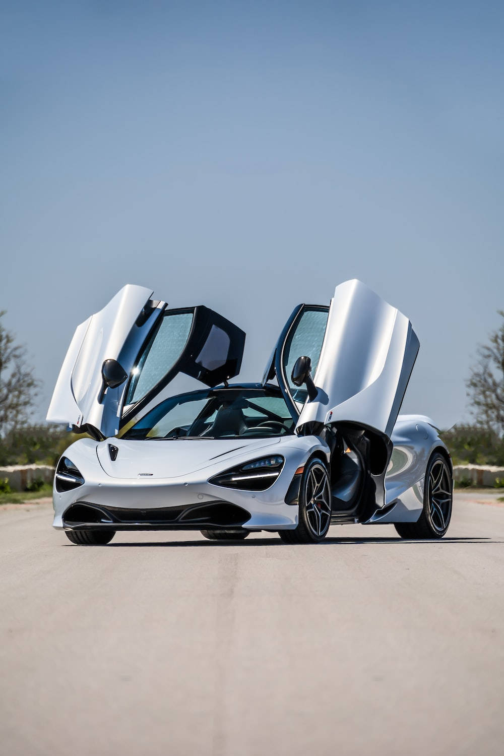 跑車 桌布 壁紙 — 一架時尚的銀色McLaren 720S超級跑車，鷗翼車門打開，停在晴朗藍天下的鋪砌道路上。