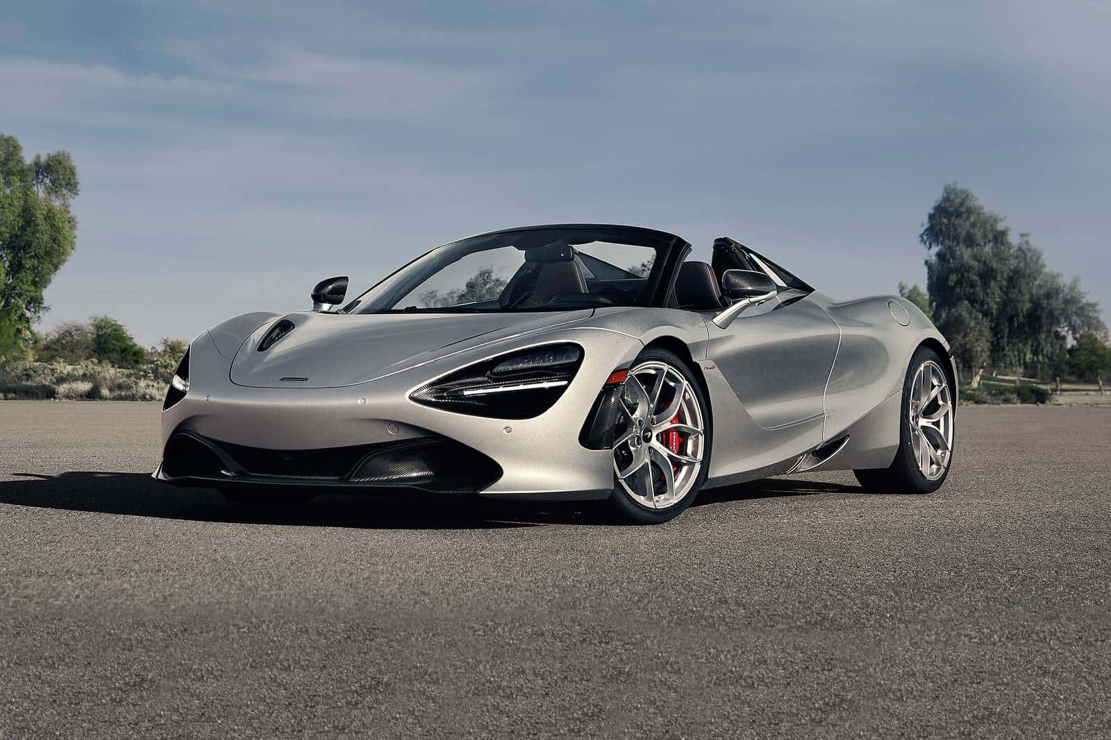 麥拉倫 桌布 壁紙 — 一架時尚的銀色McLaren 720S Spider敞篷跑車停在柏油路上，背景有樹木和晴朗的天空。
