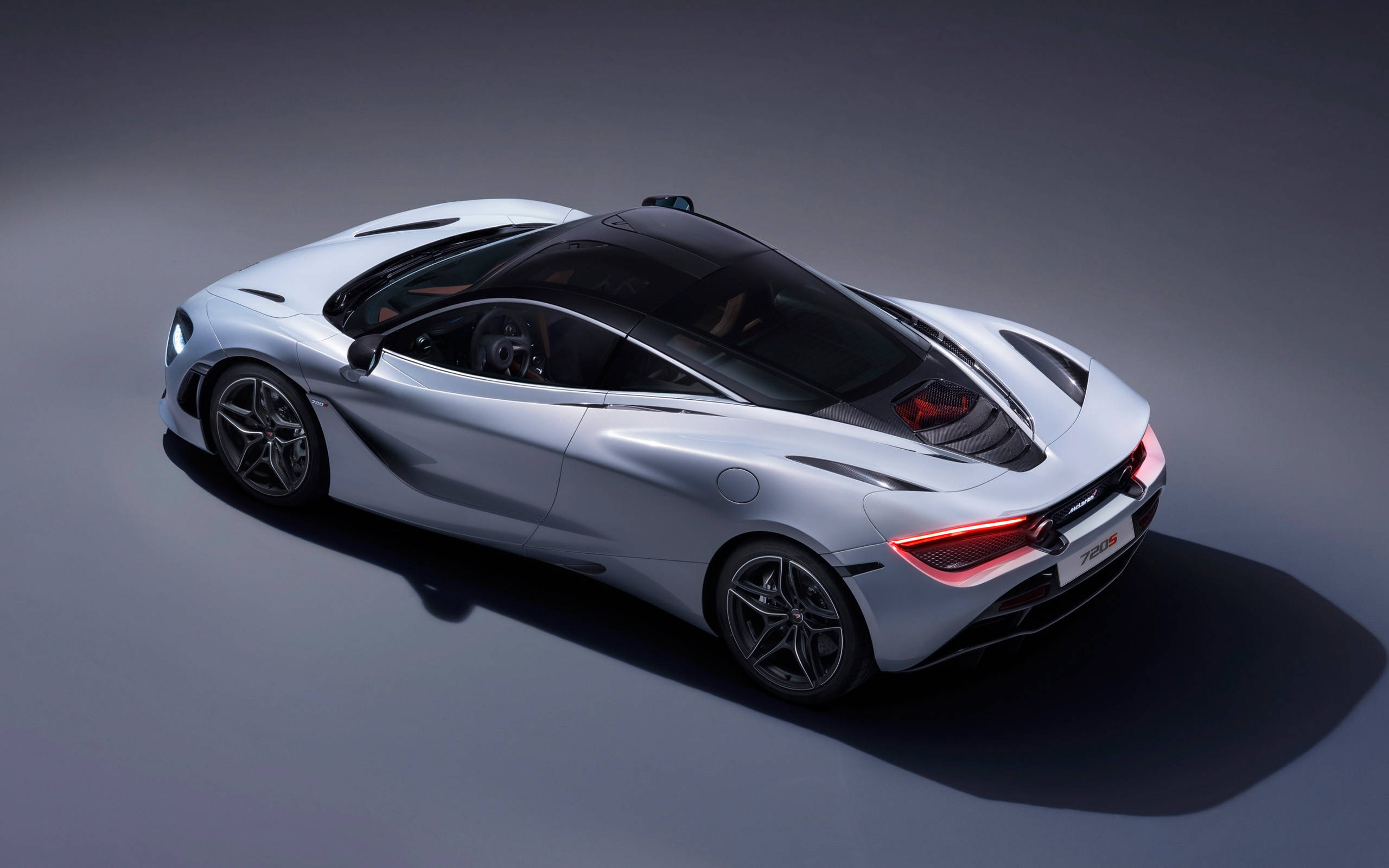 mclaren 720s 4K 桌布 壁紙 — 一架時尚的銀色McLaren 720S跑車從高角度拍攝，背景為深灰色攝影棚，燈光效果戲劇化。