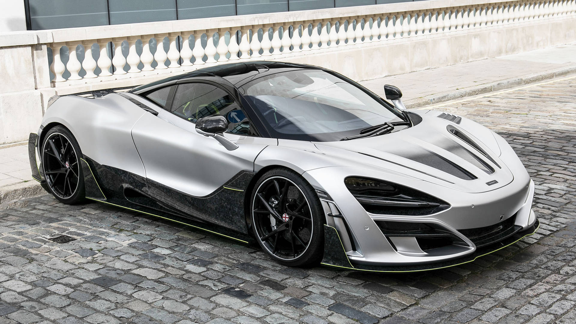 mclaren 720s 4K 桌布 壁紙 — 一架時尚的銀色McLaren Senna，帶有黑色點綴，停在石欄杆旁邊的鵝卵石街道上。
