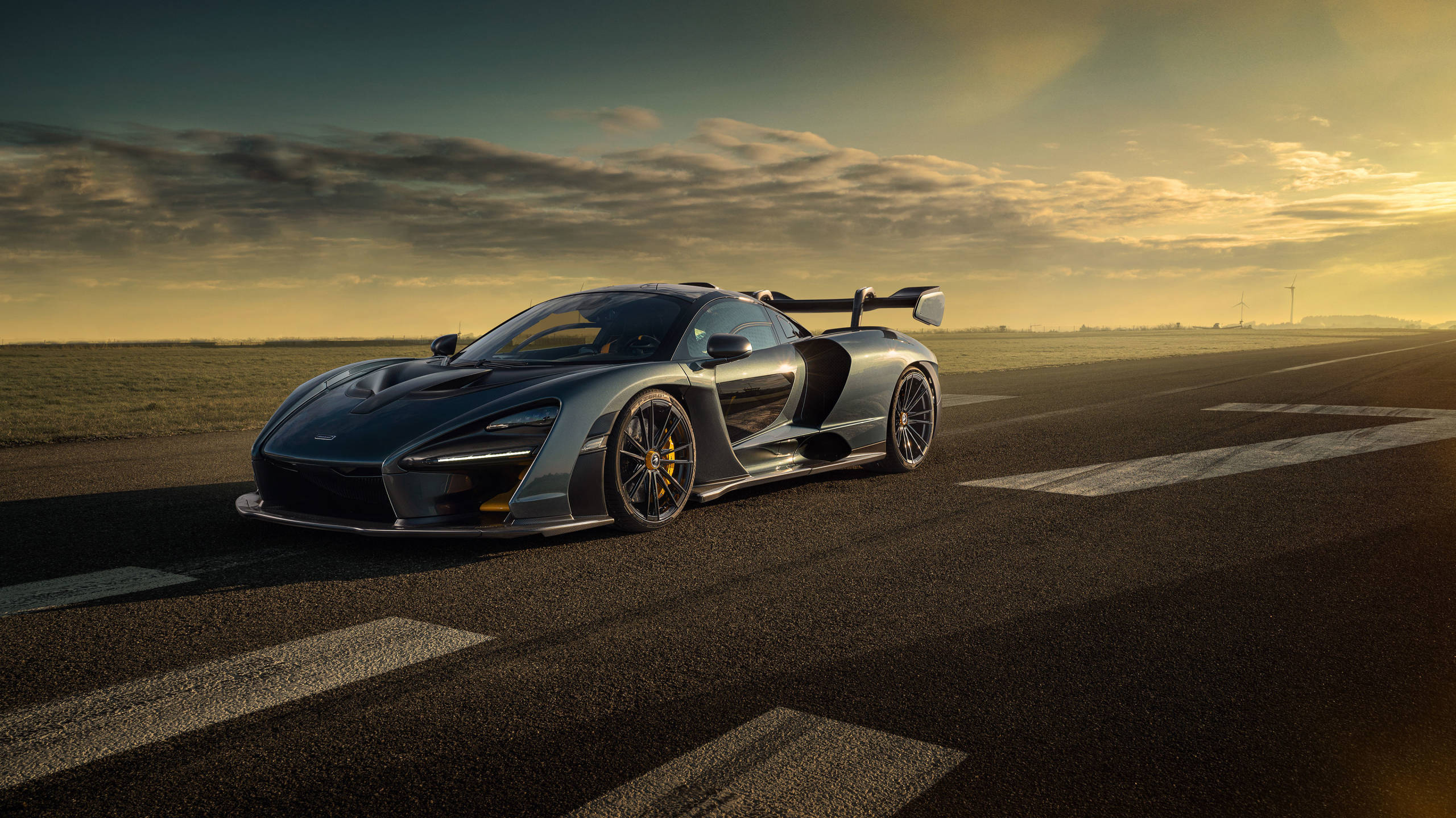 雲朵 桌布 壁紙 — 一架時尚的銀色McLaren Senna跑車停放在空曠的跑道上，正值黃金時刻，天空佈滿戲劇性的雲彩。