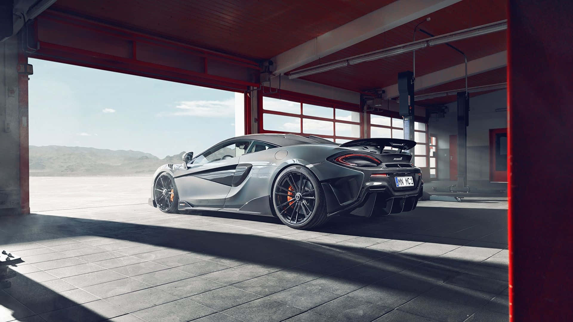 Garage 桌布 壁紙 — 一架時尚的銀色McLaren跑車停放在紅色工業車庫中，陽光從敞開的門照射進來。