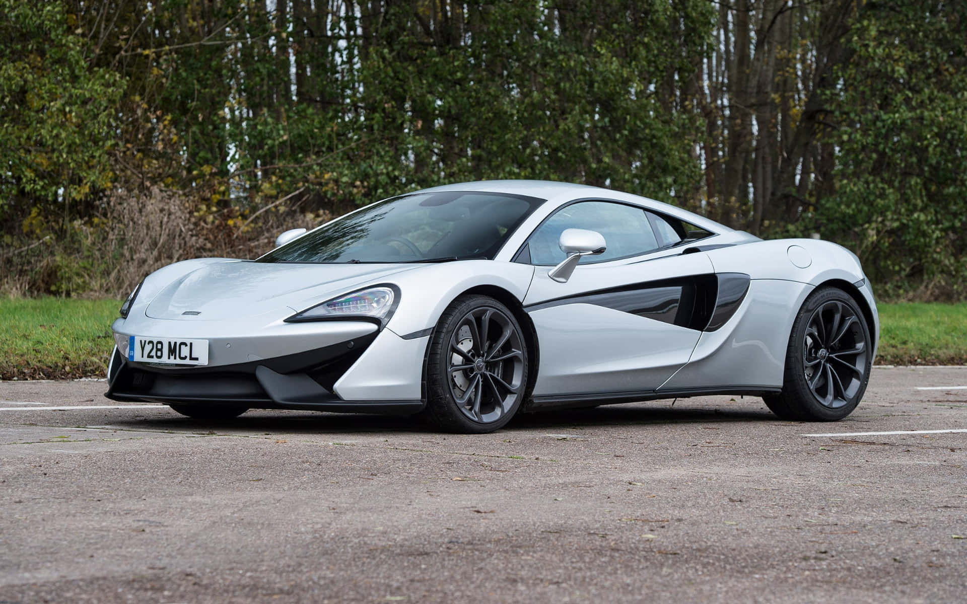 跑車 桌布 壁紙 — 一架時尚的銀色McLaren跑車停在瀝青停車場，背景有樹木。