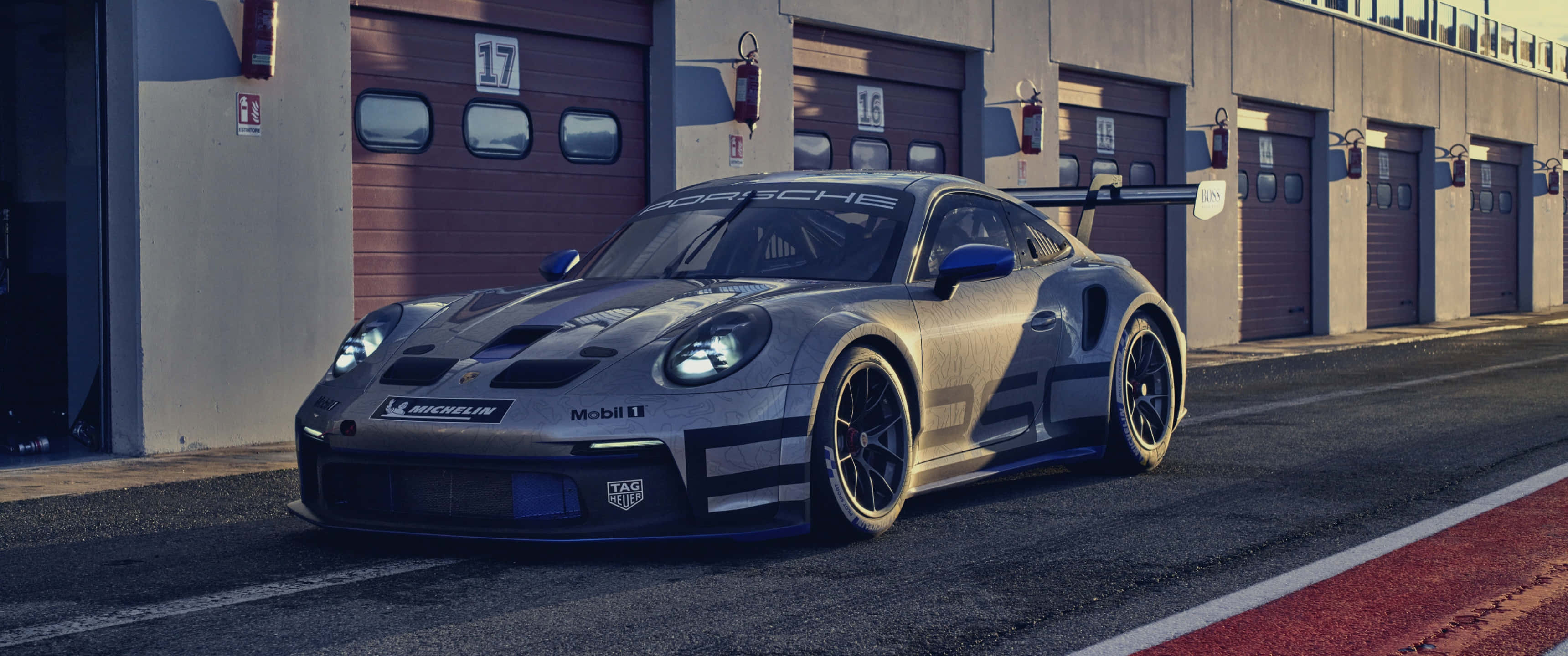 Minimalist Sports 桌布 壁紙 — 一架時尚的銀色保時捷 911 GT2 RS 賽車在金色時光的照耀下，在帶有紅色賽道邊石的維修站車庫中閃閃發光。