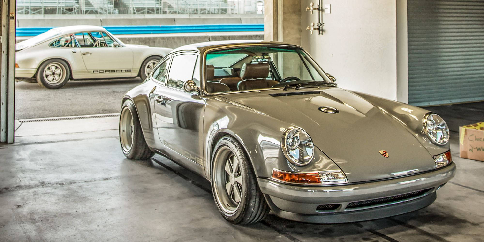 Singer 桌布 壁紙 — 一架時尚的銀色保時捷911配備寬輪胎停在車庫中，透過敞開的車門可以看到另一輛白色保時捷。