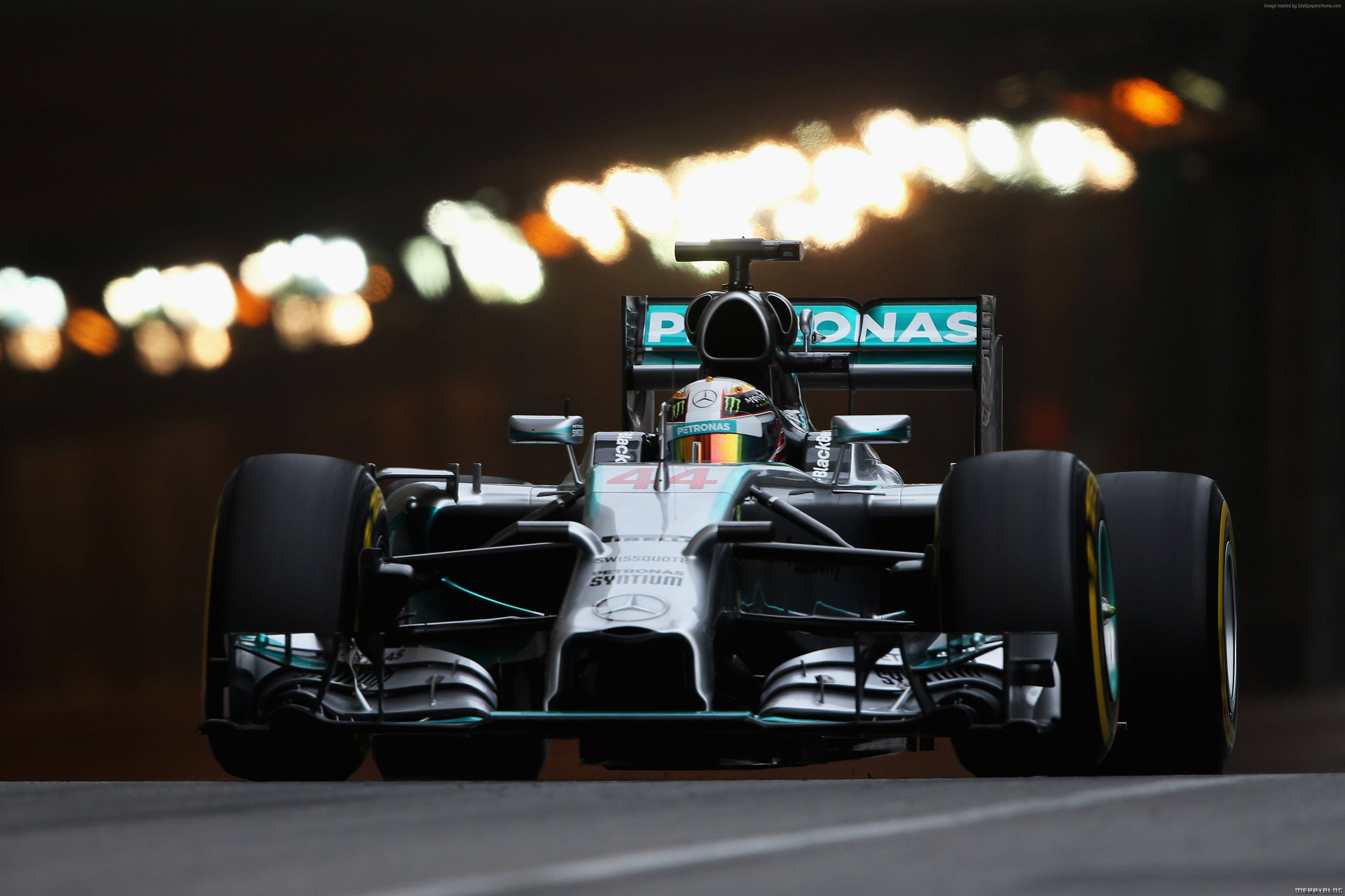 F1 桌布 壁紙 — 一架時尚的銀色和藍綠色一級方程式賽車在夜間奔馳，背景中模糊的城市燈光閃爍。