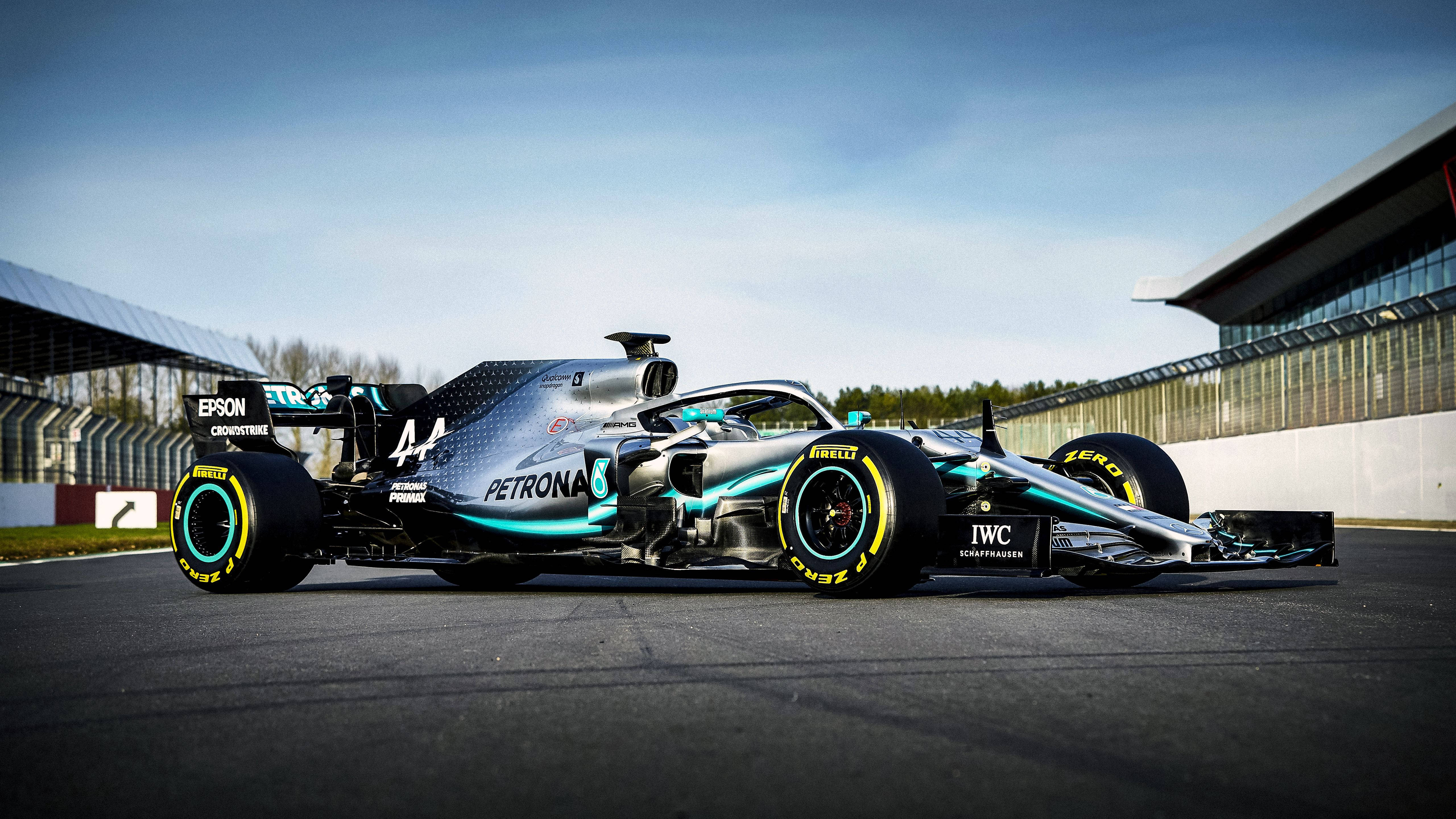 F1 桌布 壁紙 — 一架時尚的銀色和藍綠色一級方程式賽車，編號44，在晴朗的藍天下於賽道上奔馳。