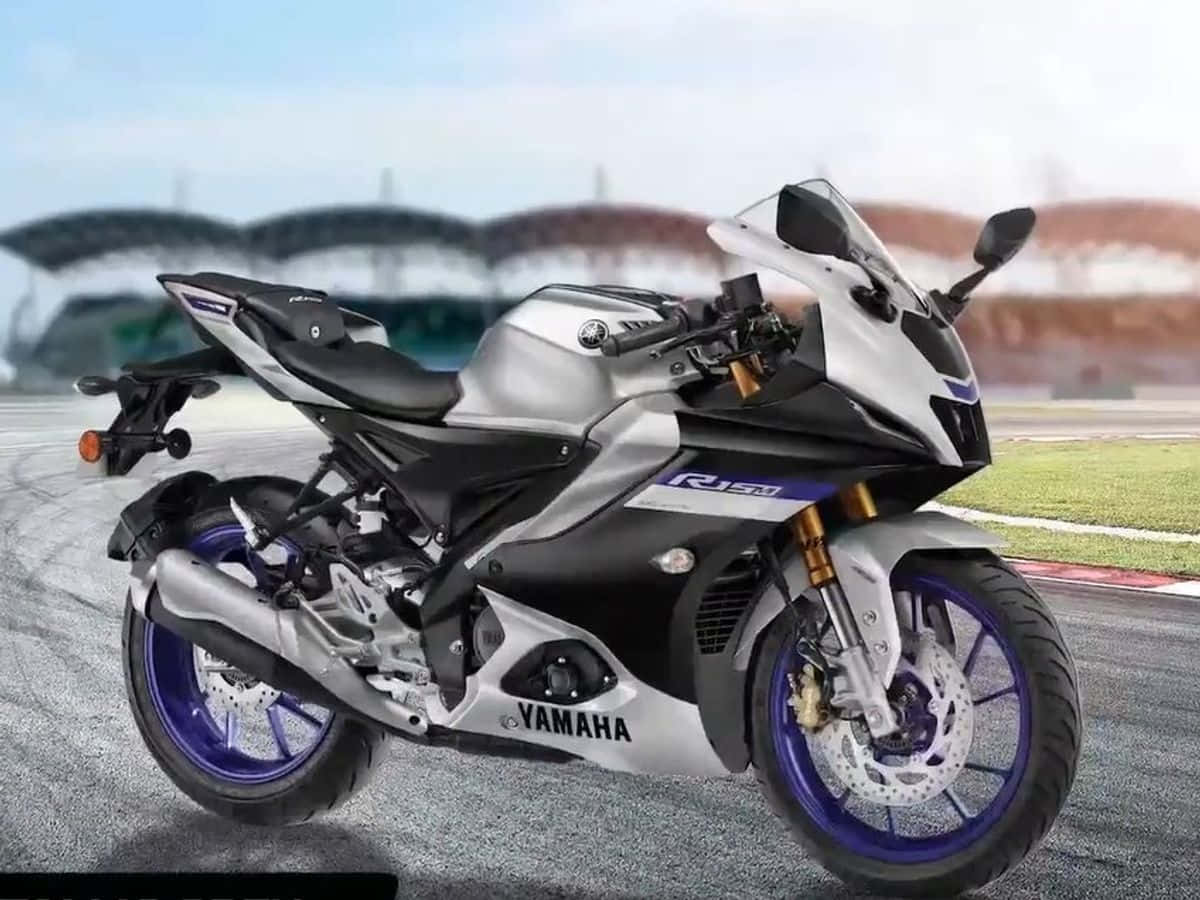 R15 桌布 壁紙 — 一架時尚的銀色和黑色Yamaha R15V3機車，配紫色輪圈，在明亮的天空下停在賽道上。