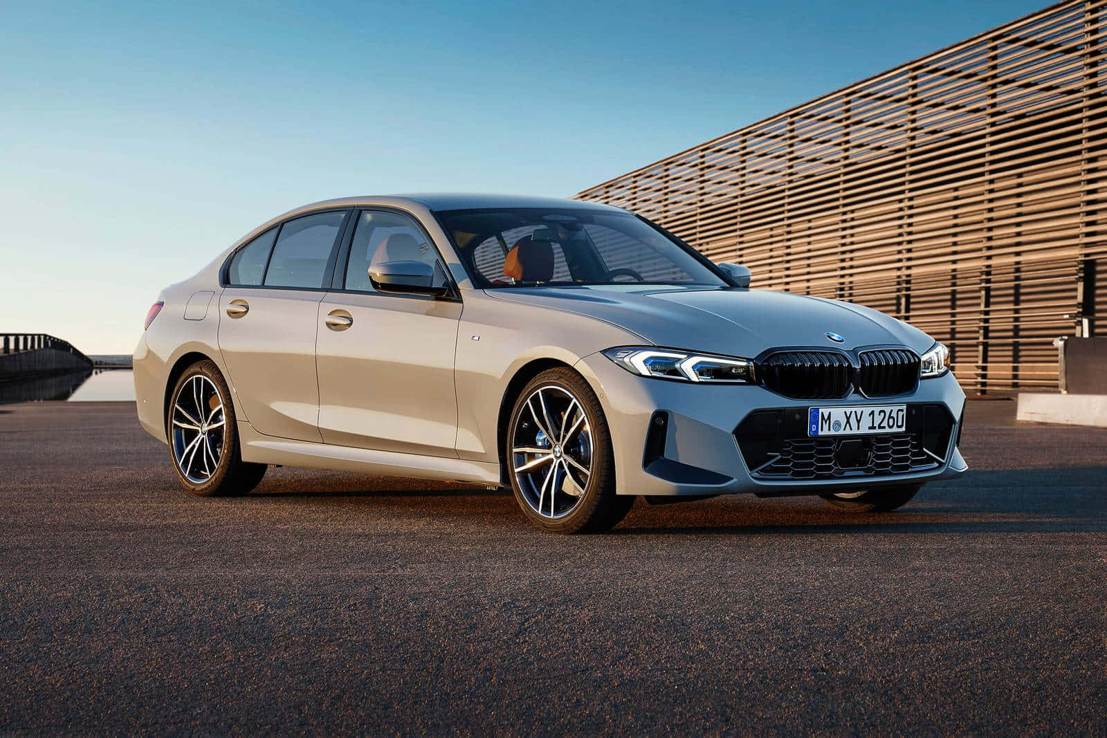 BMW 動圖 桌布 壁紙 — 一架時尚的銀色寶馬3系房車停泊在瀝青路上，旁邊是木條牆，上方是清澈的藍天。