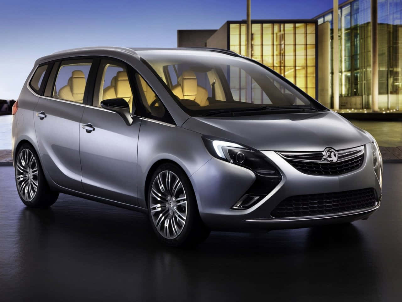 Opel Zafira 桌布 壁紙 — 一架時尚的銀色小型貨車配米色內裝，在黃昏時停在一棟現代玻璃建築前。
