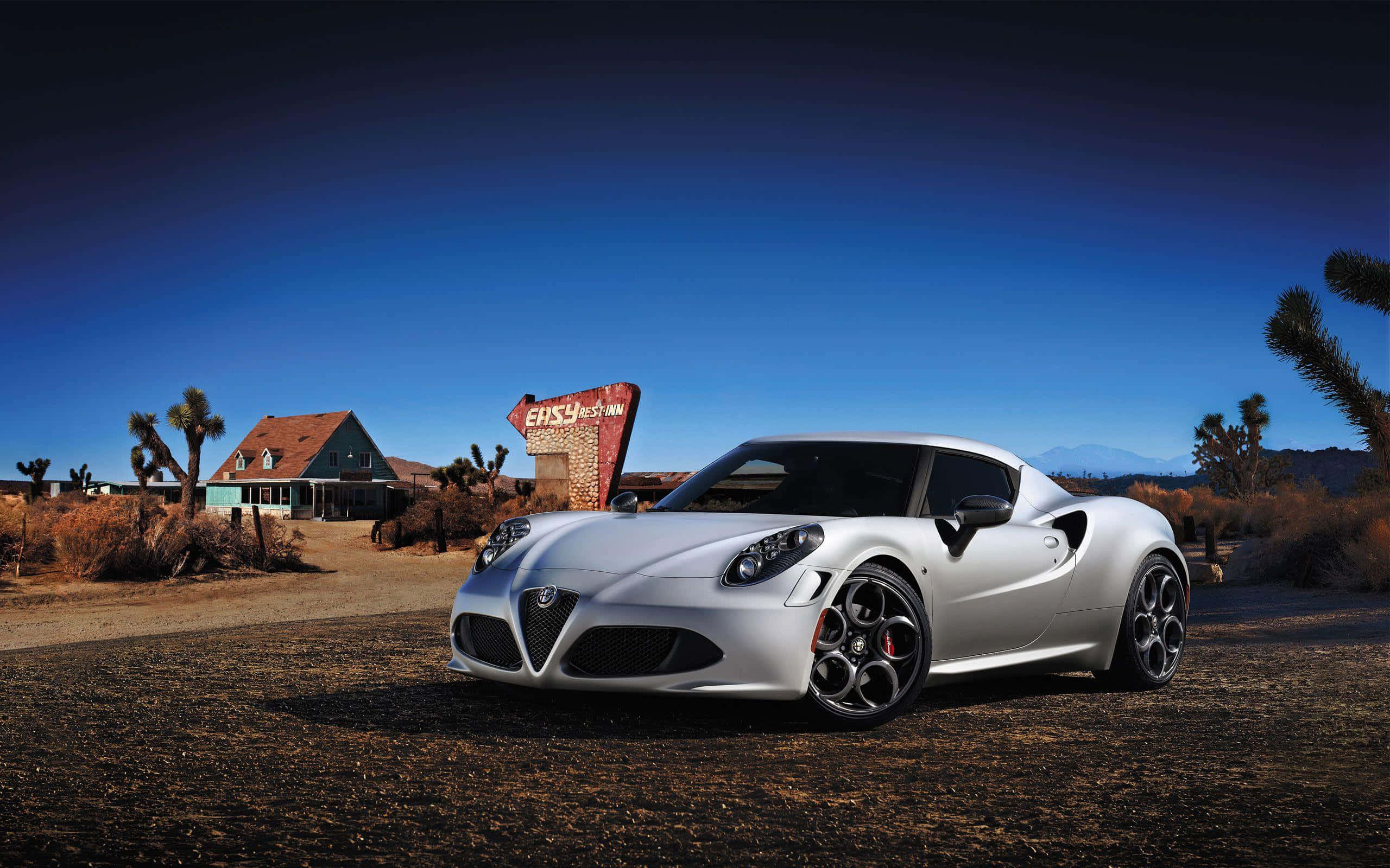 Alfa Romeo 4c 桌布 壁紙 — 一架時尚的銀色愛快羅密歐跑車停泊在沙漠景觀中，旁邊有一個復古的「Easy Inn」標誌，在清澈的藍天下。