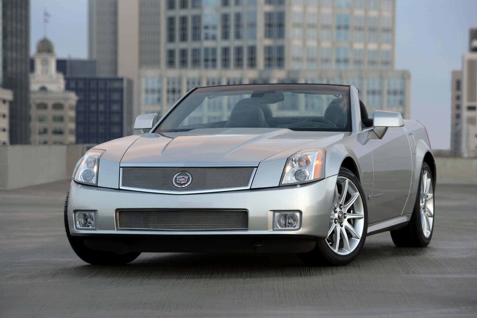 Cadillac Xlr 桌布 壁紙 — 一架時尚的銀色敞篷跑車停放在屋頂上，背景是城市天際線。