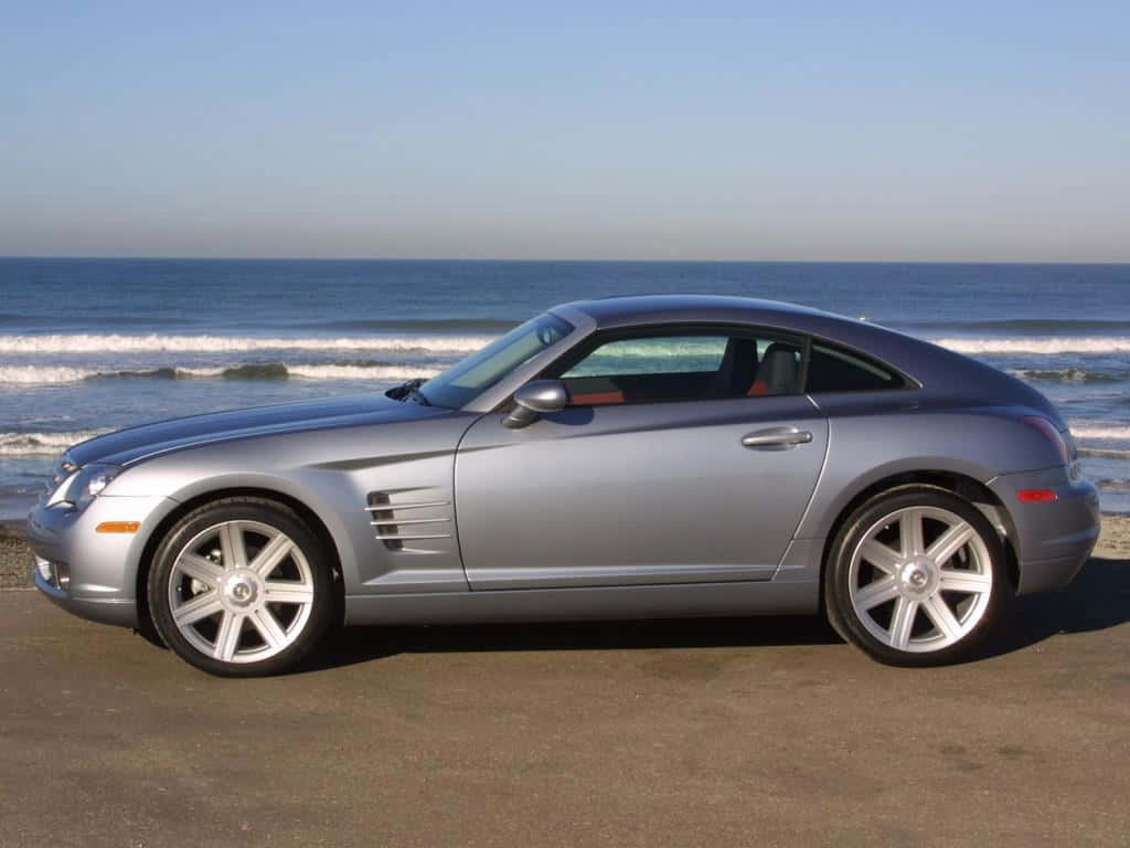 Chrysler Crossfire 桌布 壁紙 — 一架時尚的銀色敞篷跑車停泊在沙灘上，背後有海浪拍打，天空晴朗蔚藍。