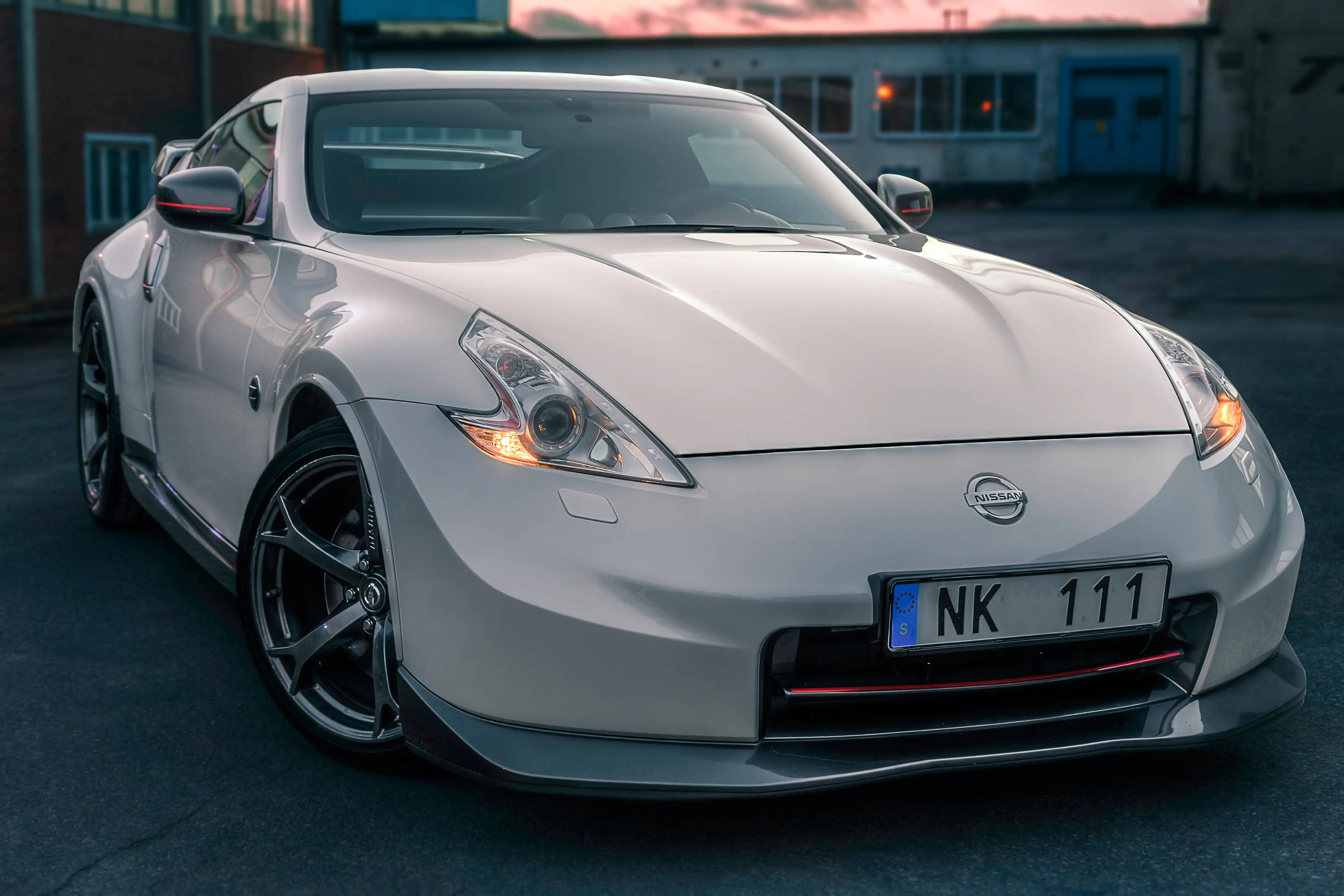 Nissan 桌布 壁紙 — 一架時尚的銀色日產370Z跑車在暮色中閃耀，配以發光的車頭燈和紅色飾條。