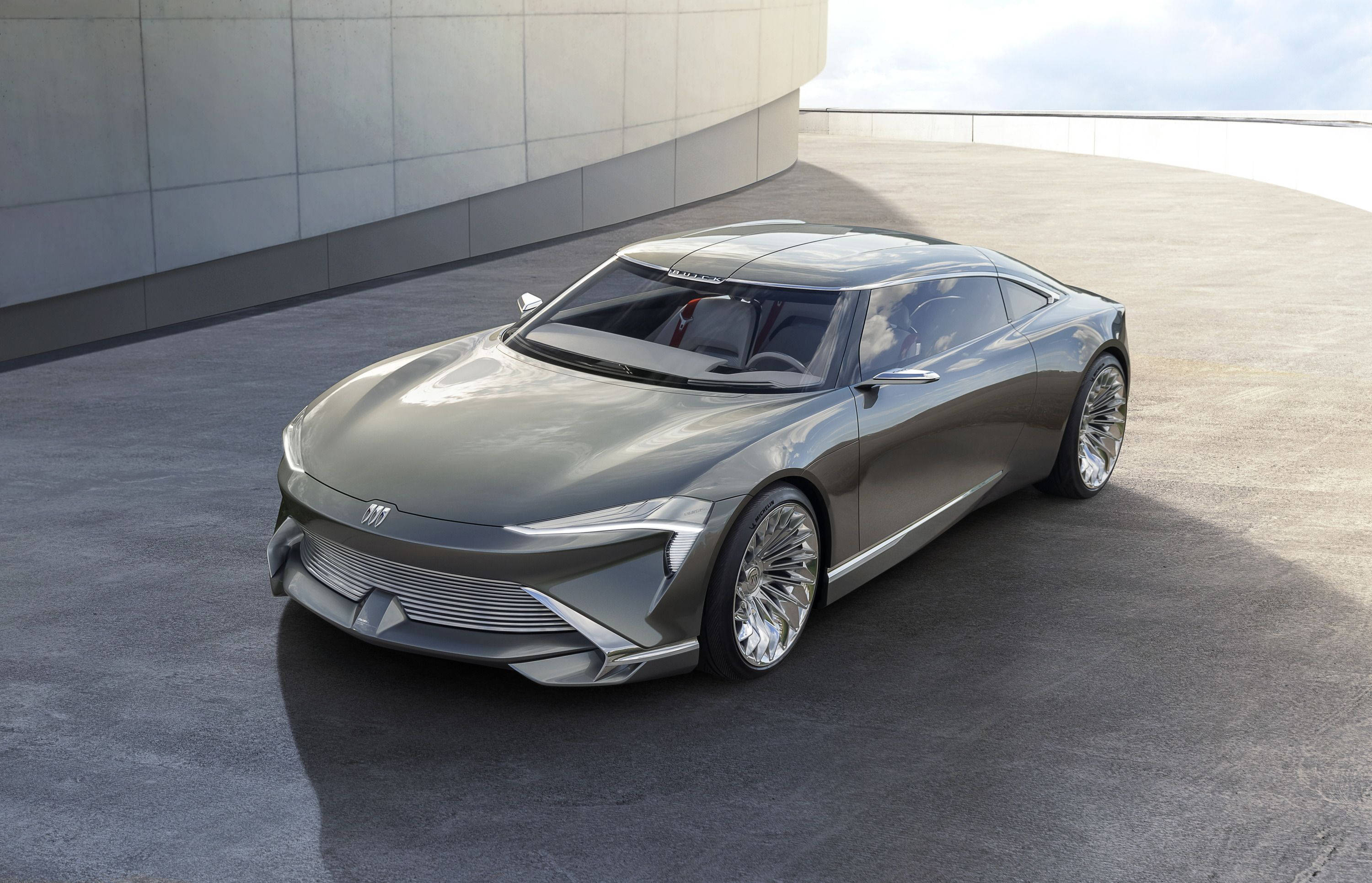 Buick 桌布 壁紙 — 一架時尚的銀色未來感跑車，配備發光車頭燈，停泊在現代彎曲牆壁旁的彎曲混凝土平台上。