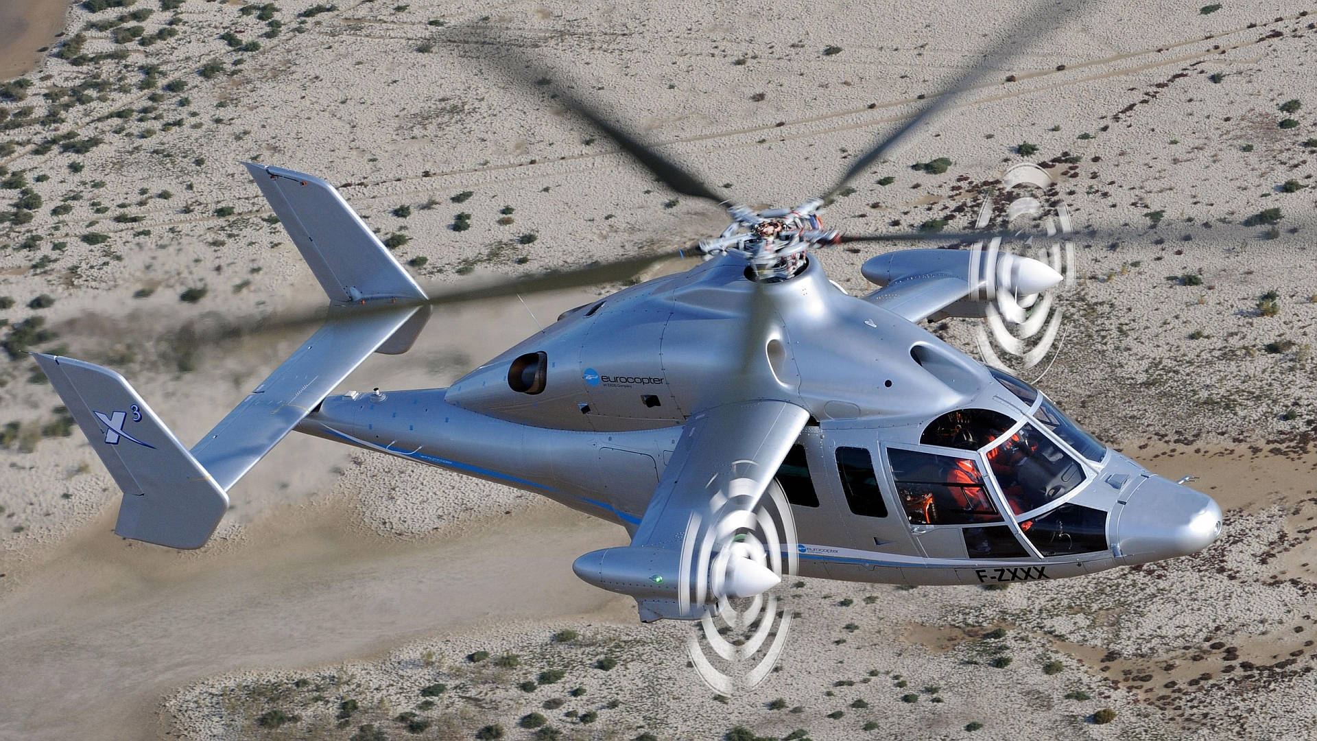 helicopter 4K 桌布 壁紙 — 一架時尚的銀色未來派直升機在植被稀疏的貧瘠沙漠景觀上空低空盤旋。