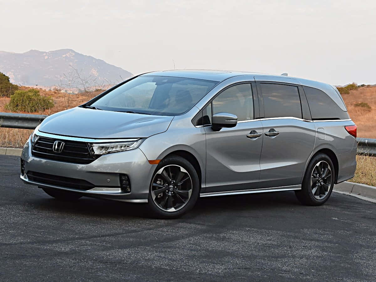 Honda Odyssey 桌布 壁紙 — 一架時尚的銀色本田奧德賽小型貨車停放在瀝青路上，背景有山脈和乾燥灌木。