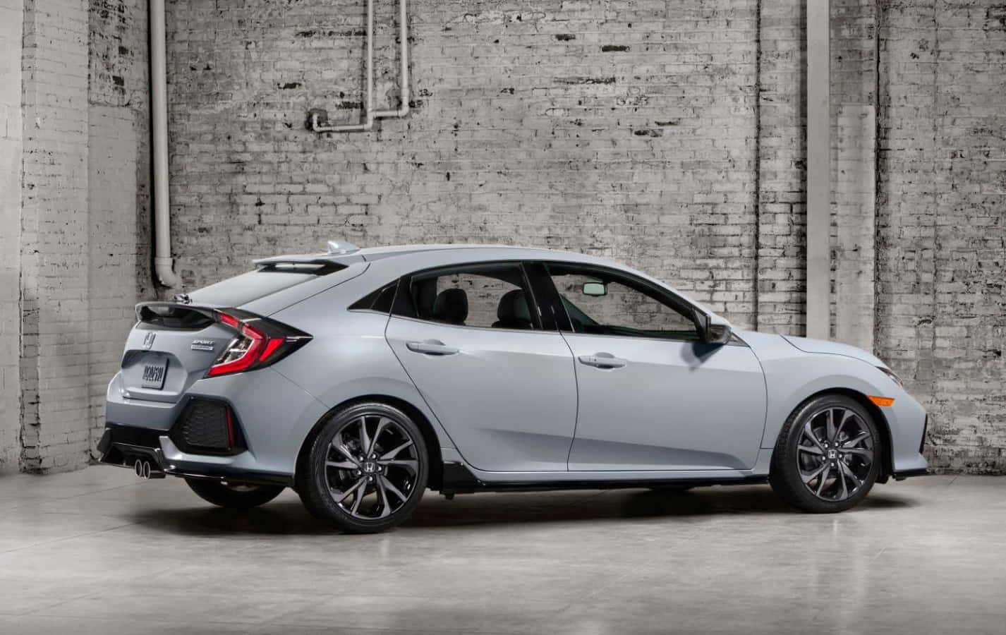 Honda Civic 桌布 壁紙 — 一架時尚的銀色本田思域掀背車停放在簡約工業車庫的風化磚牆旁。