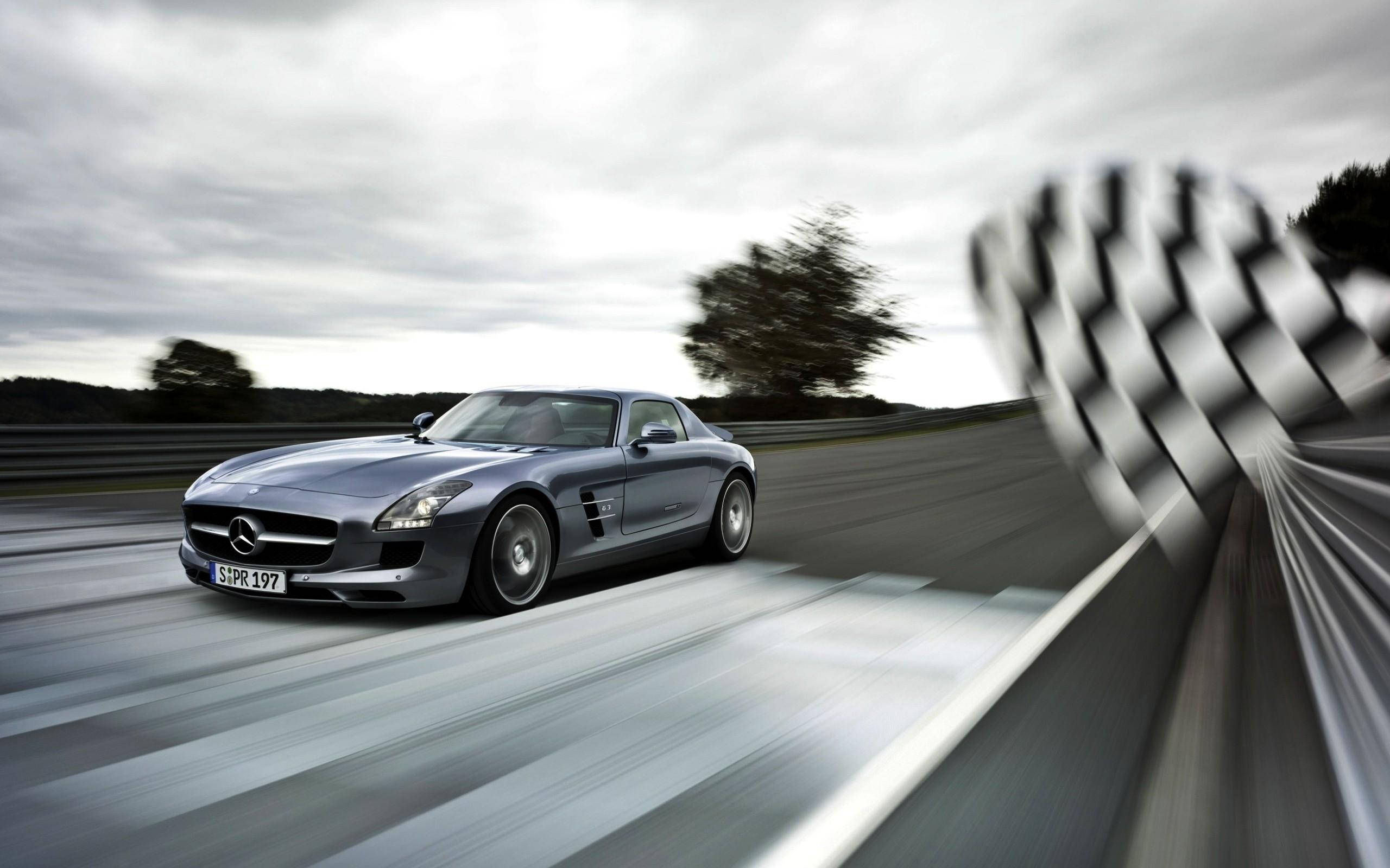 Checkered Flag 桌布 壁紙 — 一架時尚的銀色梅賽德斯 SLS AMG 在賽道上疾馳，帶有動態模糊效果，前景中格子旗旋轉。