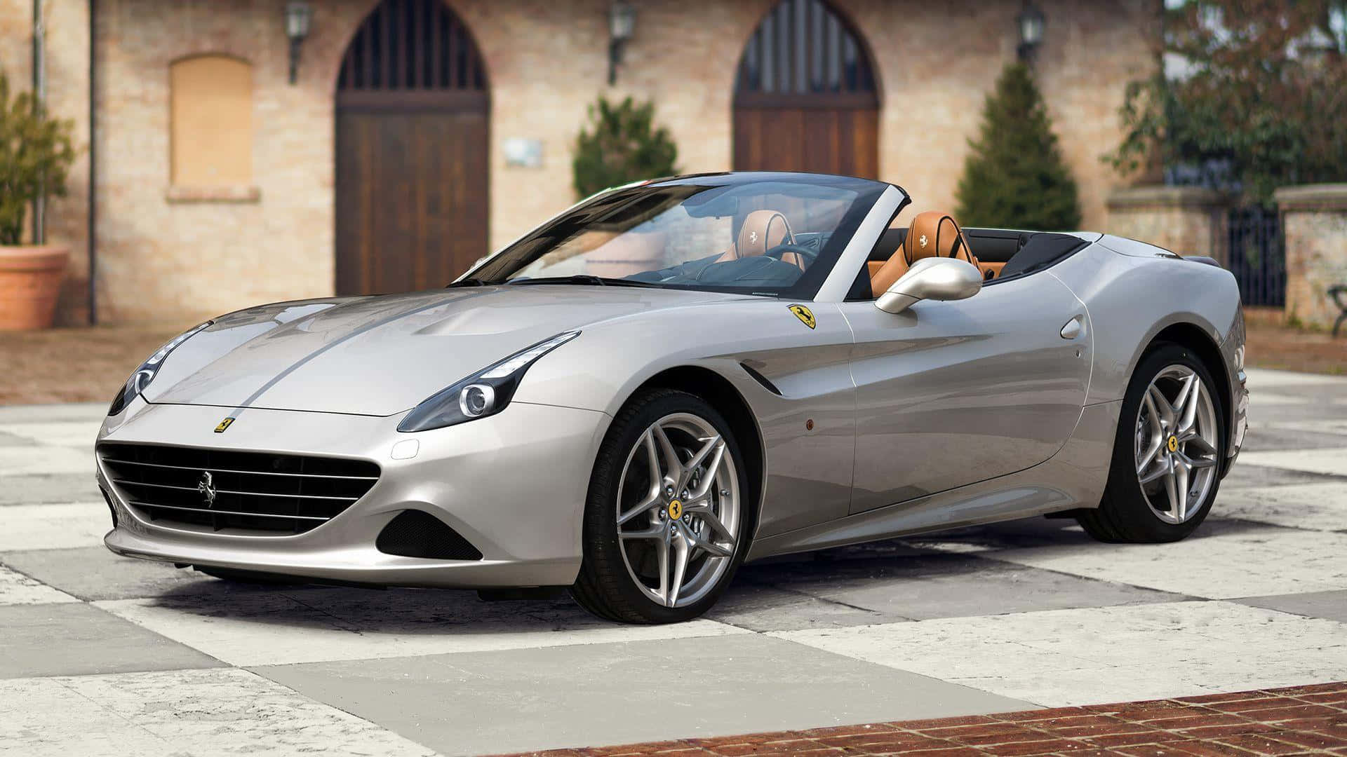 Ferrari California T 桌布 壁紙 — 一架時尚的銀色法拉利敞篷車停放在棋盤花紋的石頭車道上，前面是一座質樸的磚砌別墅。