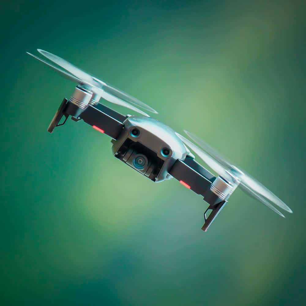 drone 桌布 壁紙 — 一架時尚的銀色無人機在柔和的綠色漸變背景上懸停，帶有發光的紅色燈光。
