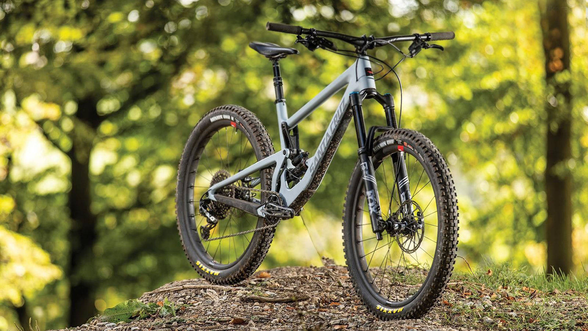 Mountain Bike 桌布 壁紙 — 一架時尚的銀色登山車矗立在森林小徑的土丘上，沐浴在透過茂密綠樹灑落的金色陽光中。
