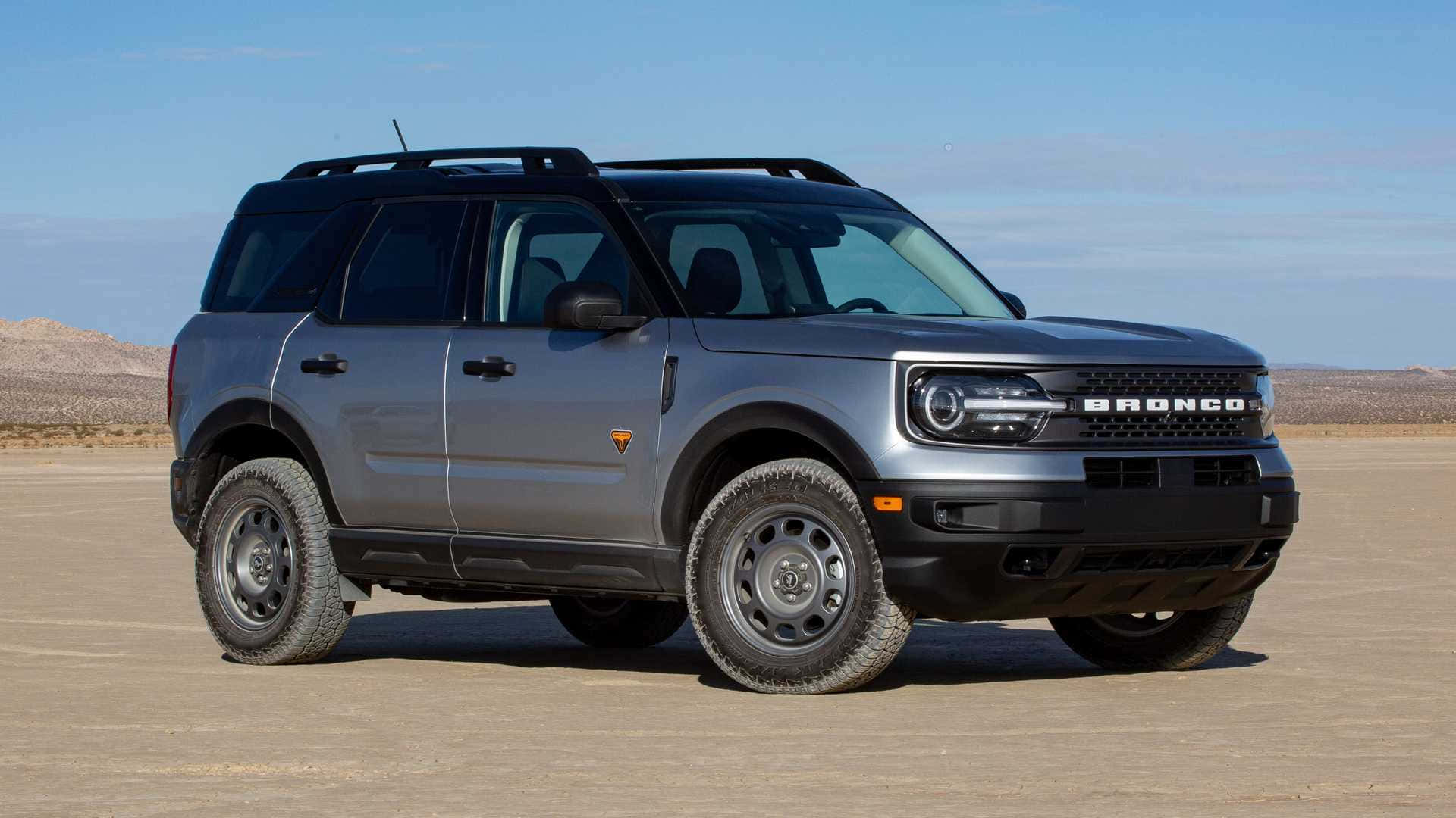 福特野馬越野車 桌布 壁紙 — 一架時尚的銀色福特Bronco SUV在晴朗藍天下，立於廣闊沙漠平原，遠方有岩石丘陵。